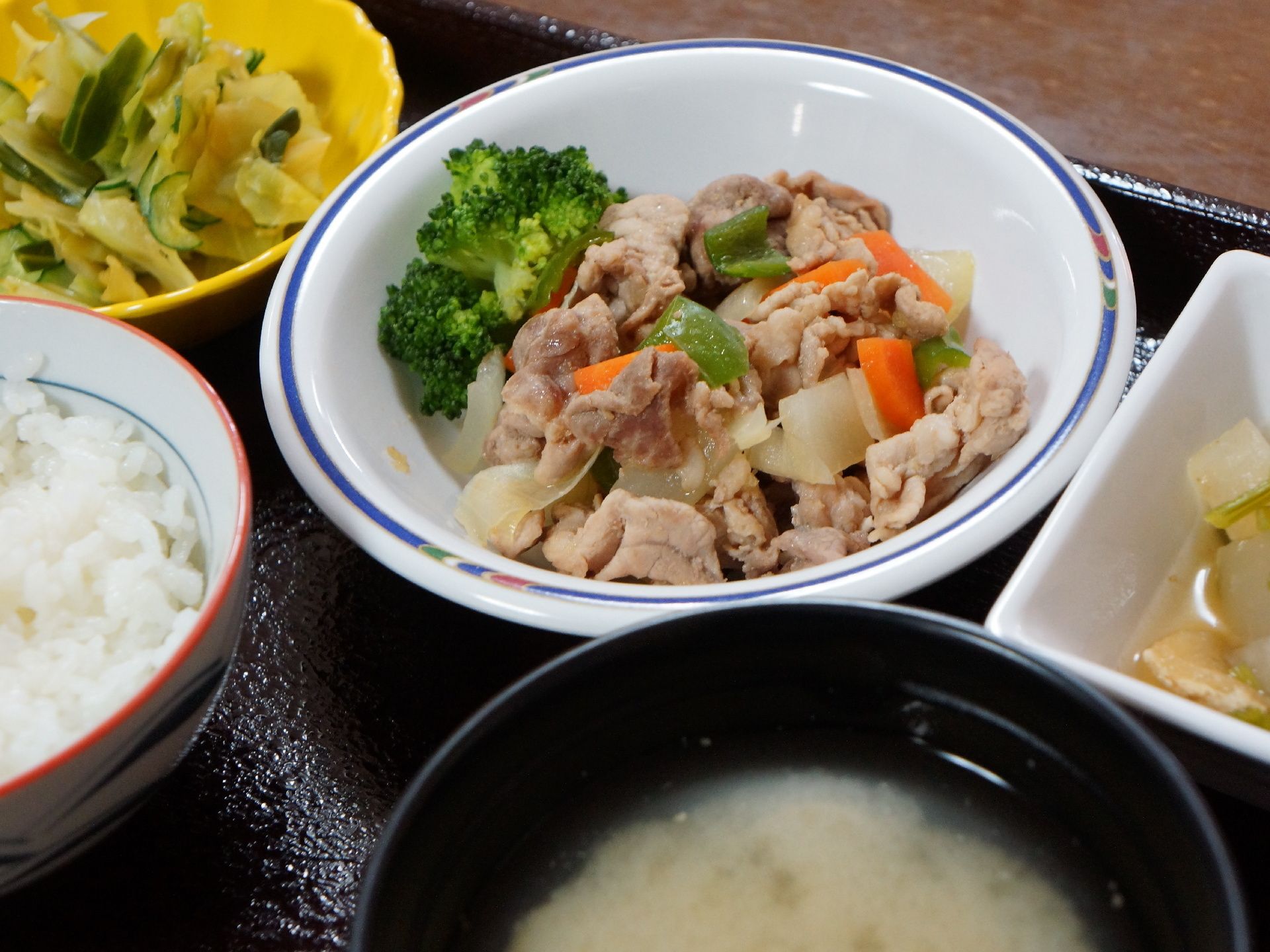 トレーに載った本日の食事のメインは、豚肉と人参、ピーマンなどの炒め煮、ブロッコリー添えである。他に2品とご飯と汁物がある。