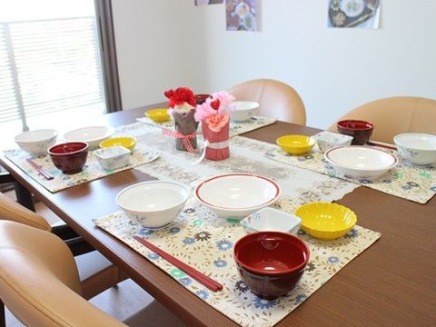 ４人用テーブルのランチョンマットの上に、茶椀や小皿などが並べられ、ご飯の用意がされている。中央にはレースのテーブルセンターが敷かれている。