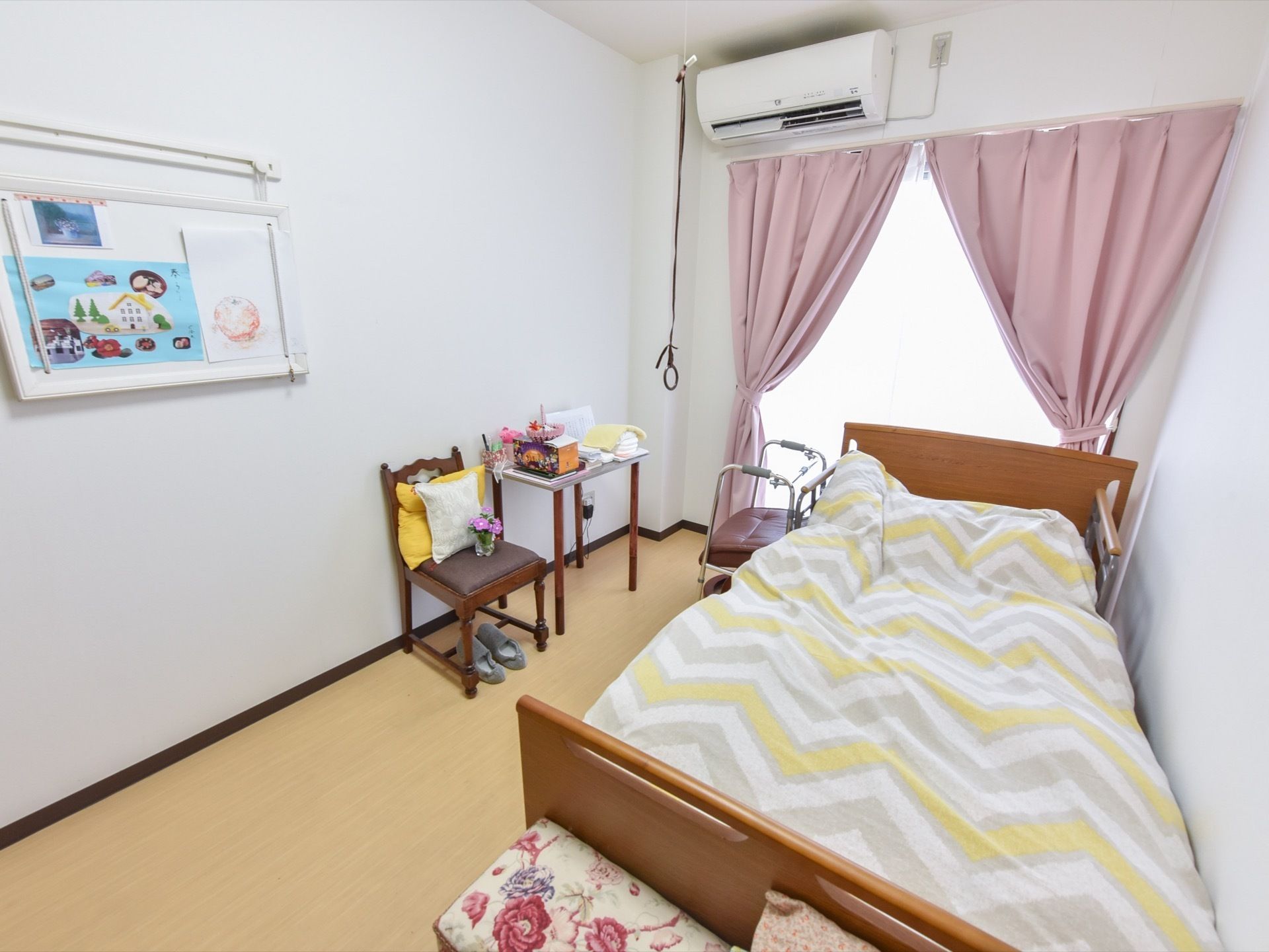 居室には介護用ベッドとテーブル、椅子が置かれている。テーブルや椅子の上には小物が置かれており、壁には製作物などが掲示されている。