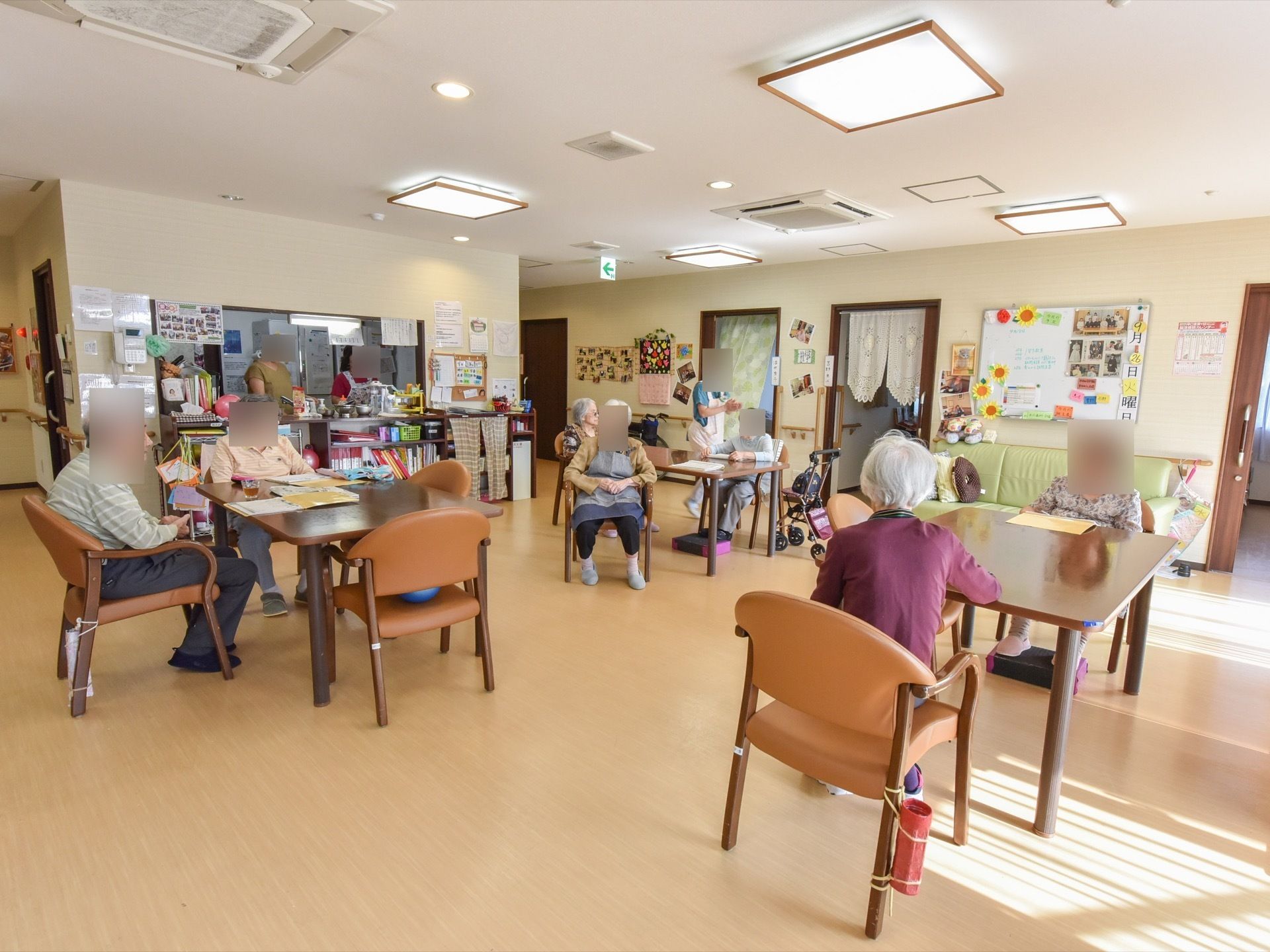 ホールには椅子やテーブルが複数台置かれており、入居者様が座って職員の話を聞いている。食事などもできるように奥にはカウンターキッチンもある。