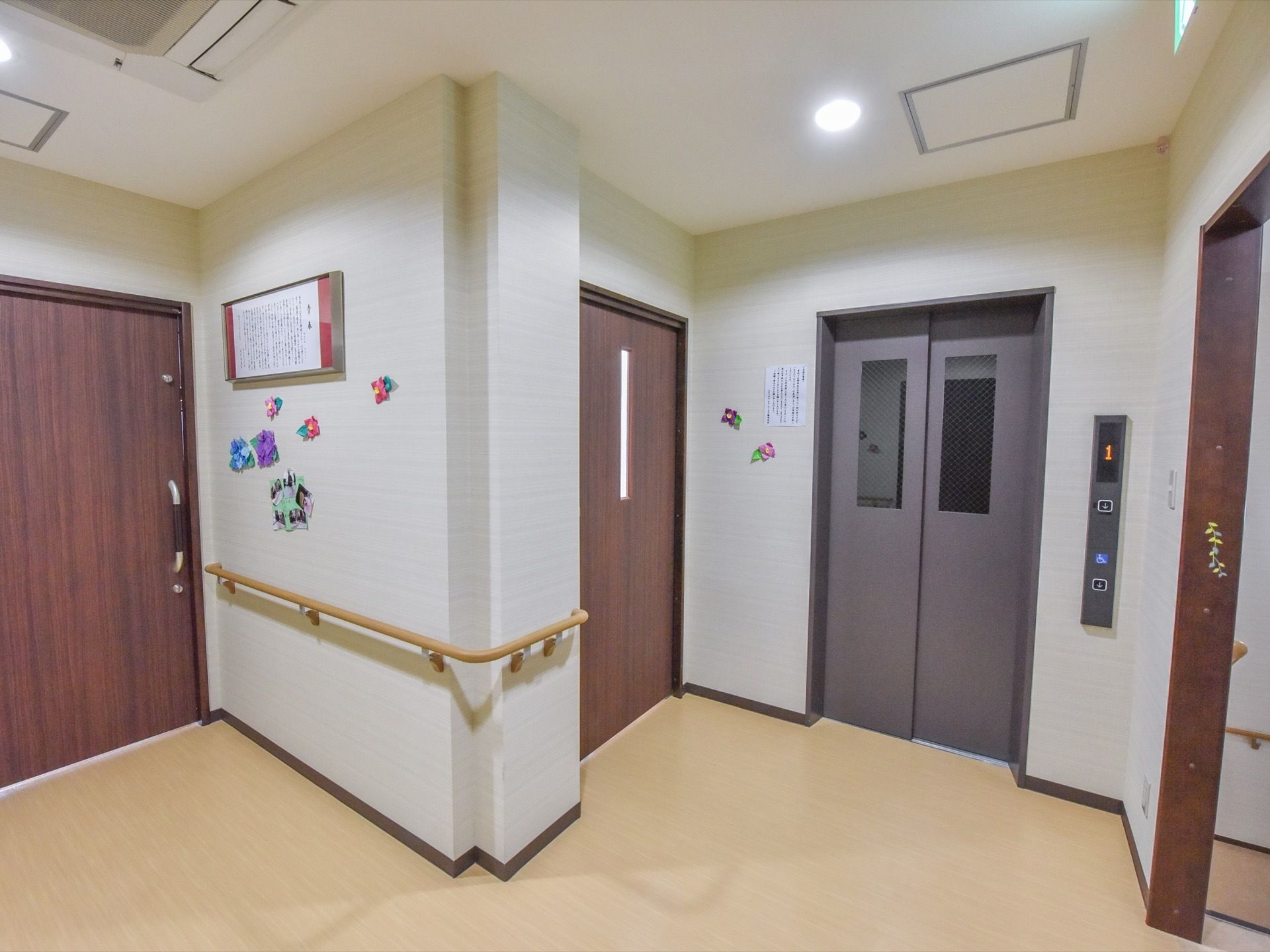 エレベーターから部屋に向かう通路には手すりが設置されている。ドアのそばの壁には、額、写真、折り紙で作られた花が飾ってある。