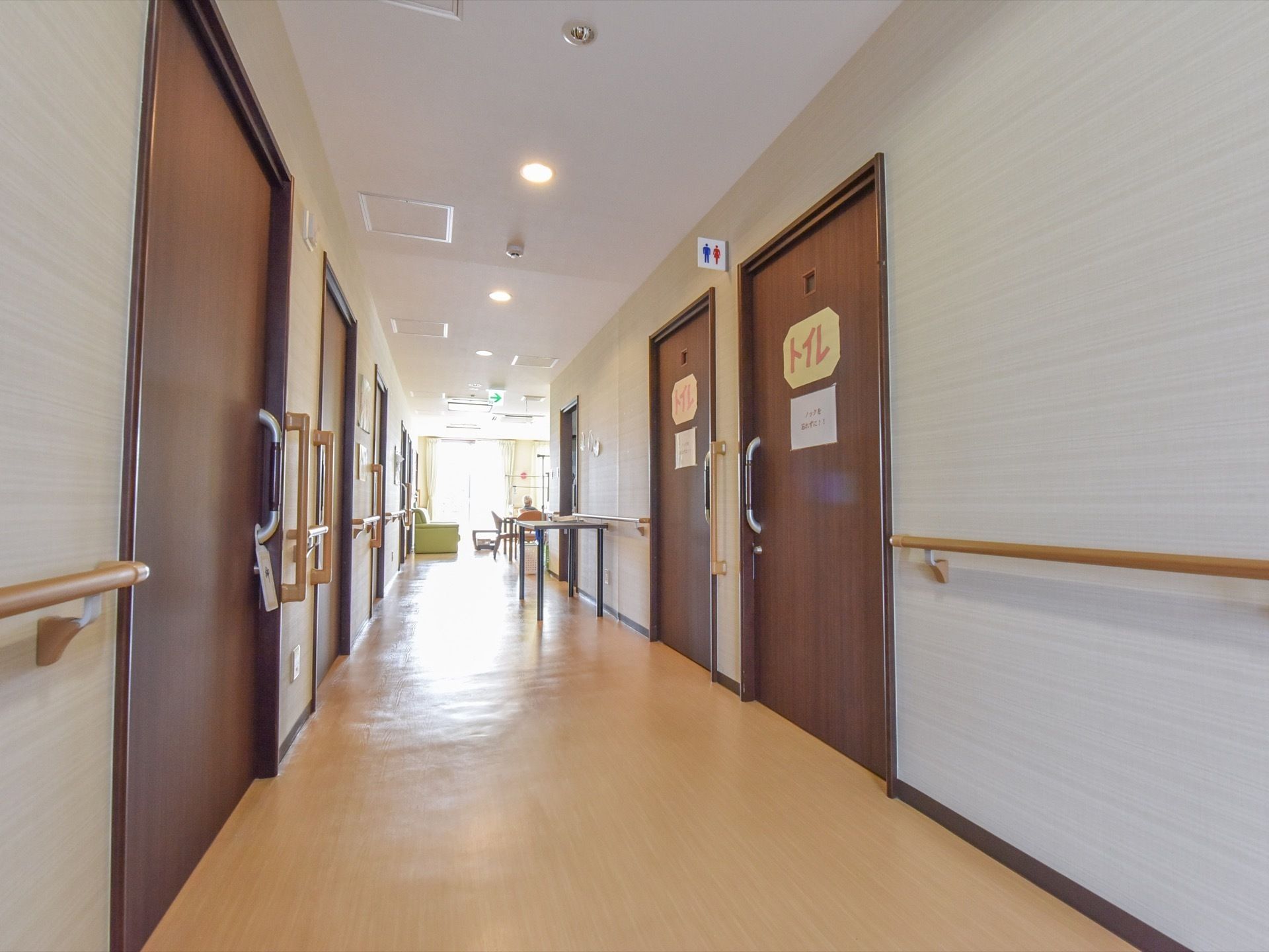 壁には手すりが完備されている。つきあたりは窓のある広い部屋につながっている。途中にテーブルが置かれている。