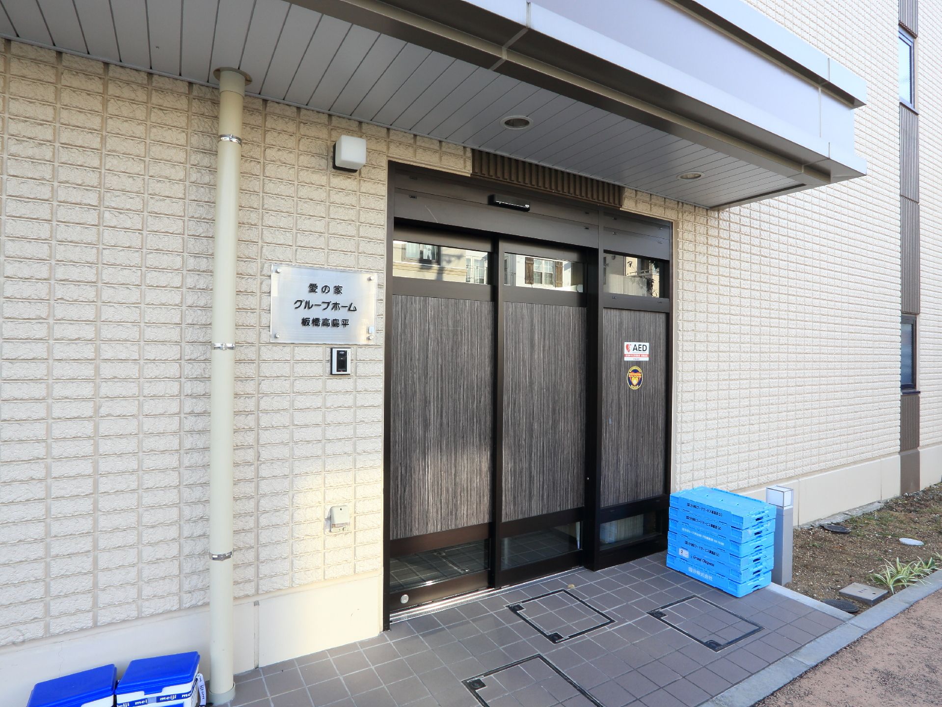愛の家グループホームの入り口の外観。自動扉の横には呼び出しチャイムが備え付けられている。自動扉は外から中が丸見えにならないようになっている。