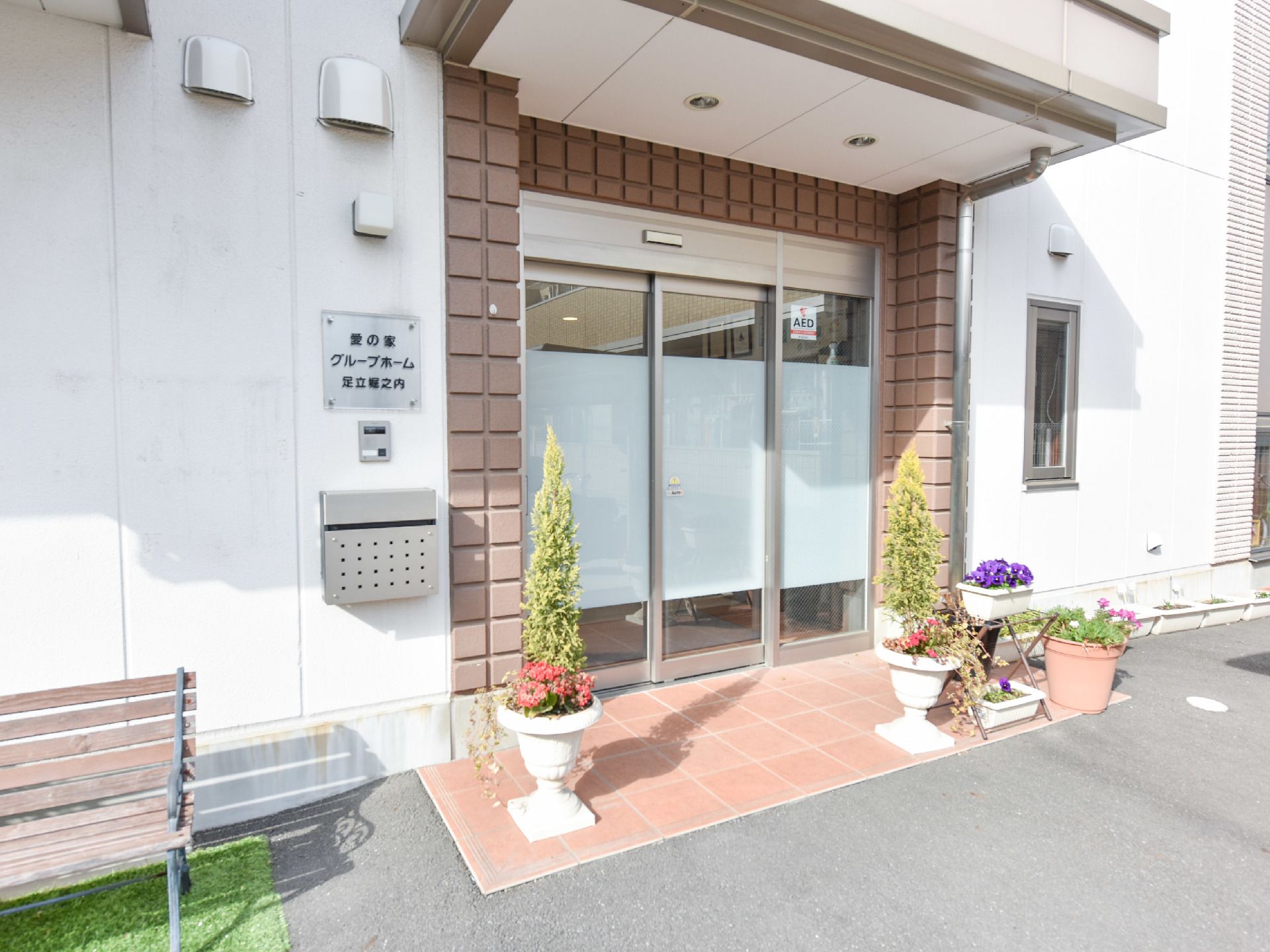 玄関はガラスの自動ドアになっており、手前にベンチや鉢植えがある。ポストが設置されており、AED除細動器のステッカーが貼ってある。