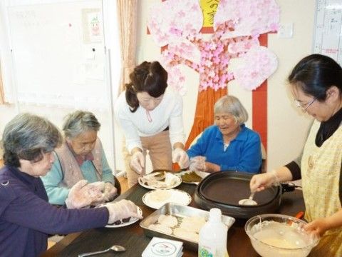 女性スタッフと一緒にホットプレートを囲んでおかず作りに取り組んでいる女性入居者様