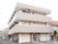 "施設外観は白っぽい3階建ての建物で、玄関の外に駐輪場、駐車場、自動販売機、傘立てがある。2