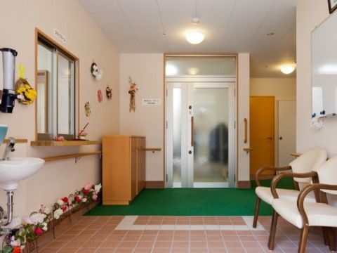 白く明るいエントランスには、花をモチーフとした飾りが置かれている。入口には手洗い用の洗面台と泥落とし用のマットを敷いている。