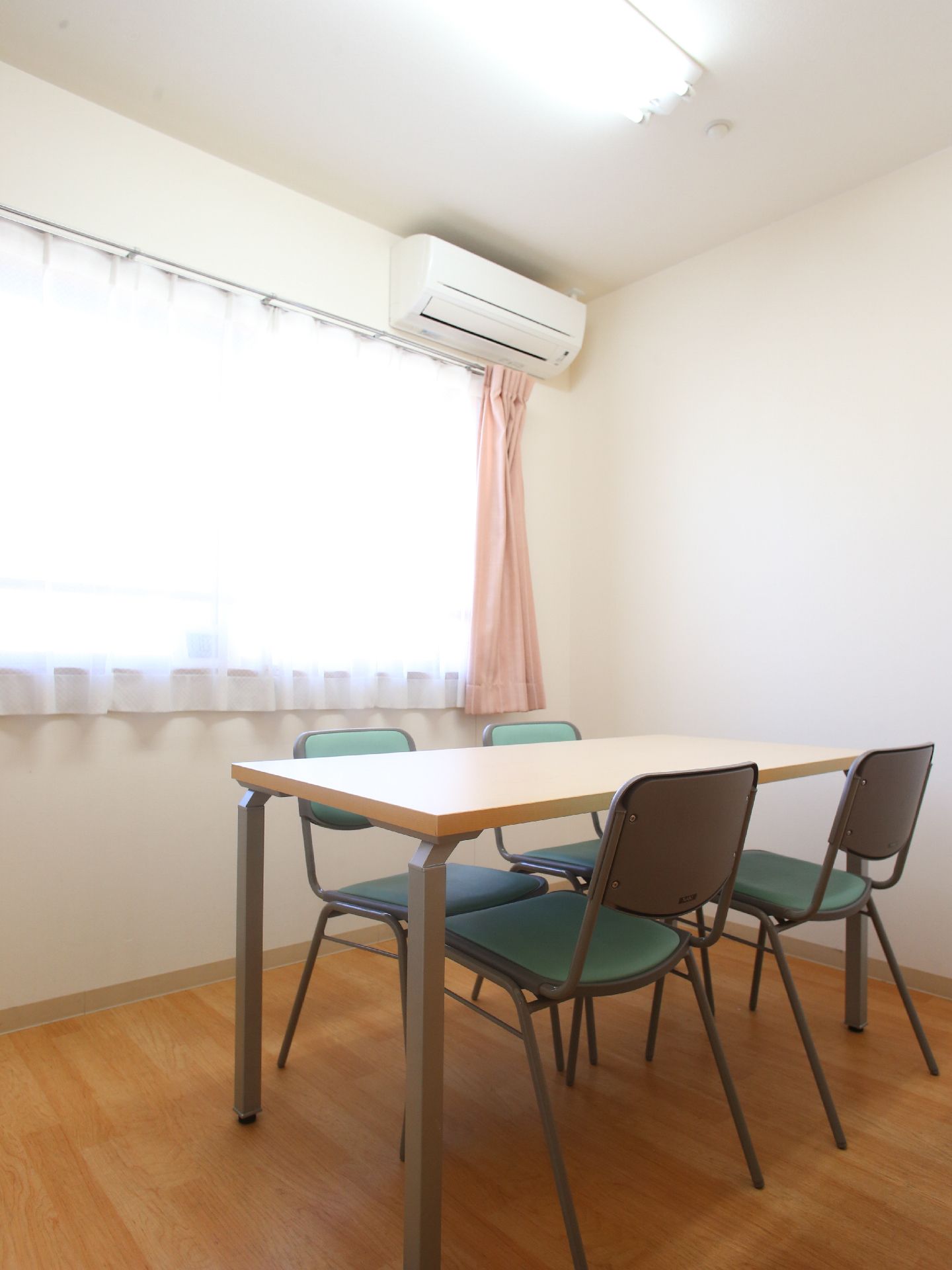 フローリングの部屋に置かれた4人掛けのテーブルセット。壁にはレースのカーテンの閉められた窓があり、明るい光が差し込む。