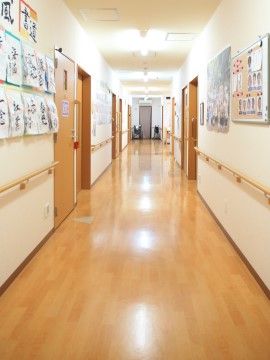 「愛の家グループホーム 練馬早宮」廊下。廊下の両壁には入居者様の作品を掲示しており、蛍光灯が灯り、明るい廊下。