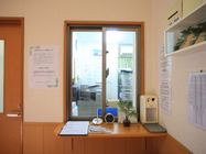 カウンターにはボールペンと記入用紙の他、時計やカレンダー、観葉植物などが置かれている。受付内には事務資料とコピー機が窓から見える。