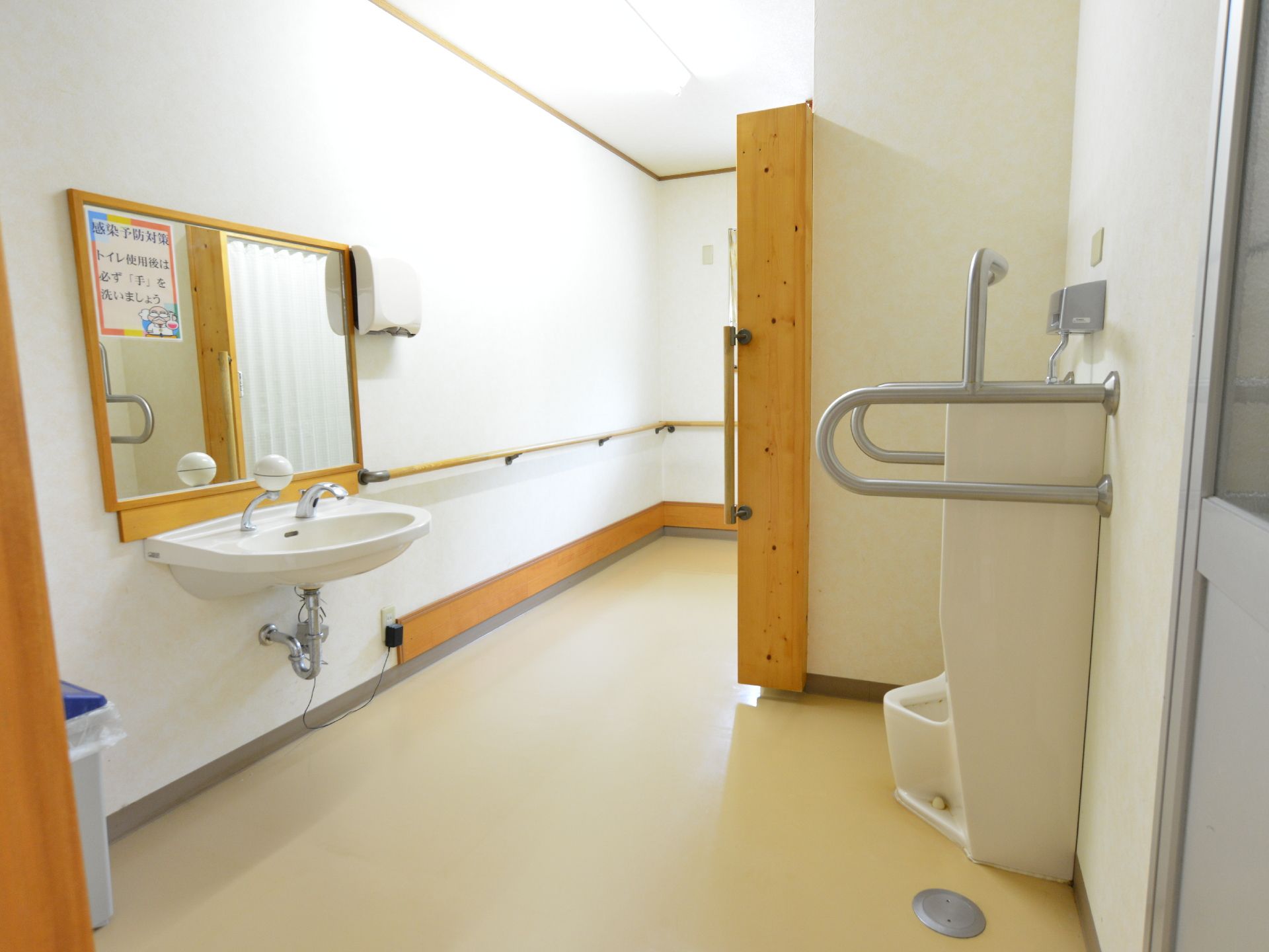 施設は共同で使用できるトイレも設置されている。奥行きがある室内は男性用小便器と洗面台、奥には個室がある。壁や便器には手すりが設置されている。