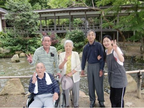 和風の建築物と池の前で写真に収まる入居者様と女性スタッフ