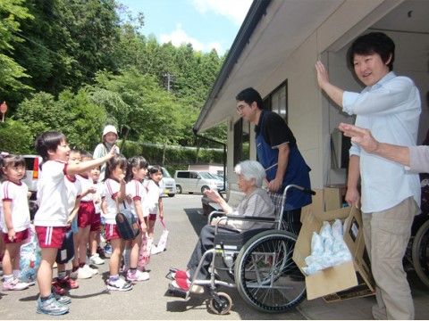 幼稚園児の訪問を受けて、車いすに座って手を振る女性入居者様