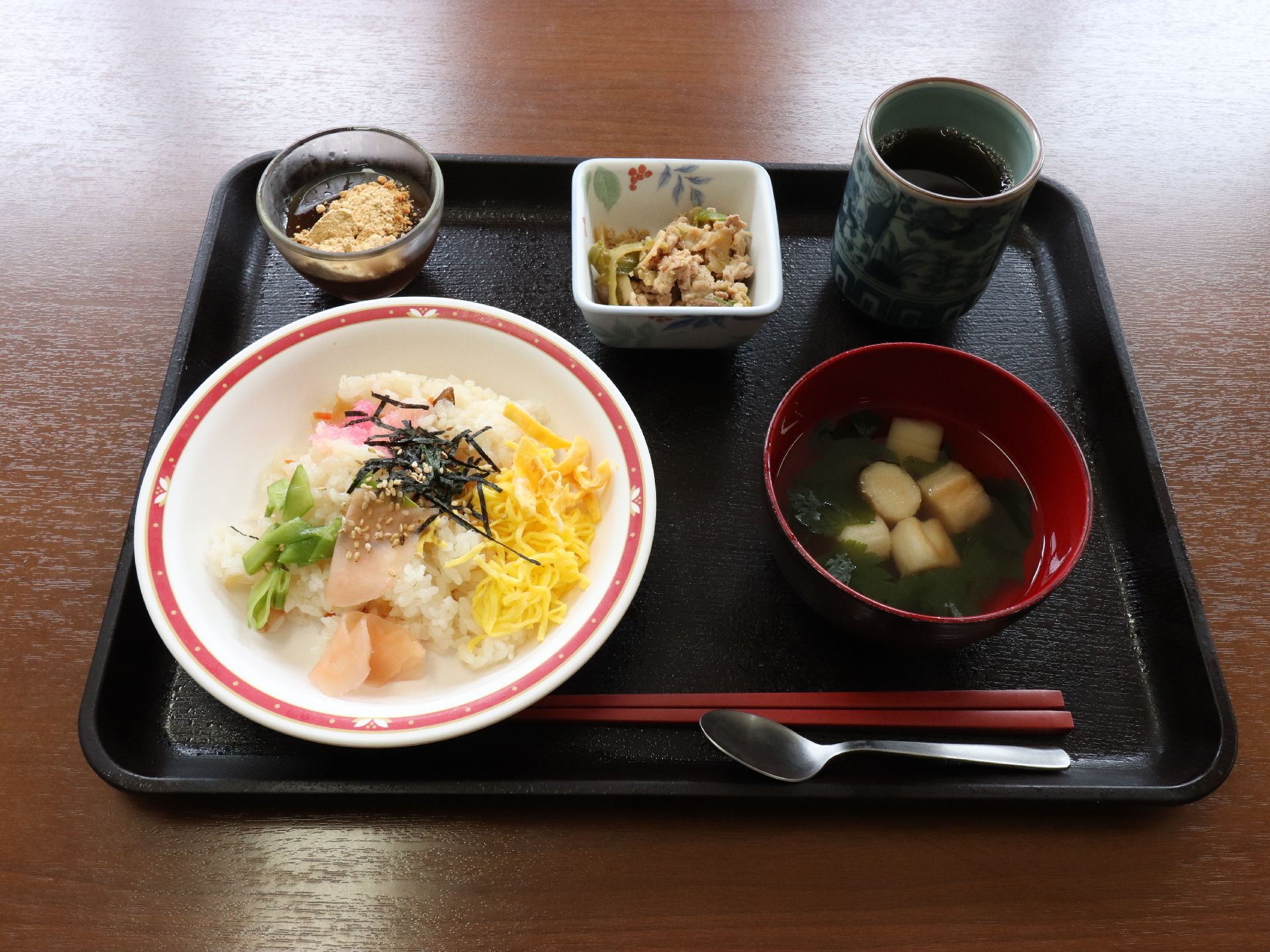 長方形のトレーの上に食事がセットされている。ちらし寿司に汁物と小鉢が付き、デザートとお茶が添えられている。