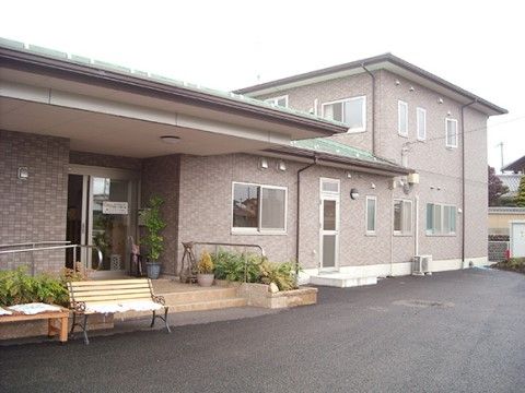 平屋と二階が繋がっており、外壁は茶系のタイル貼りで、玄関前にはベンチと縁側が並んでいる。手すり付の階段かスロープを利用して玄関に入る。