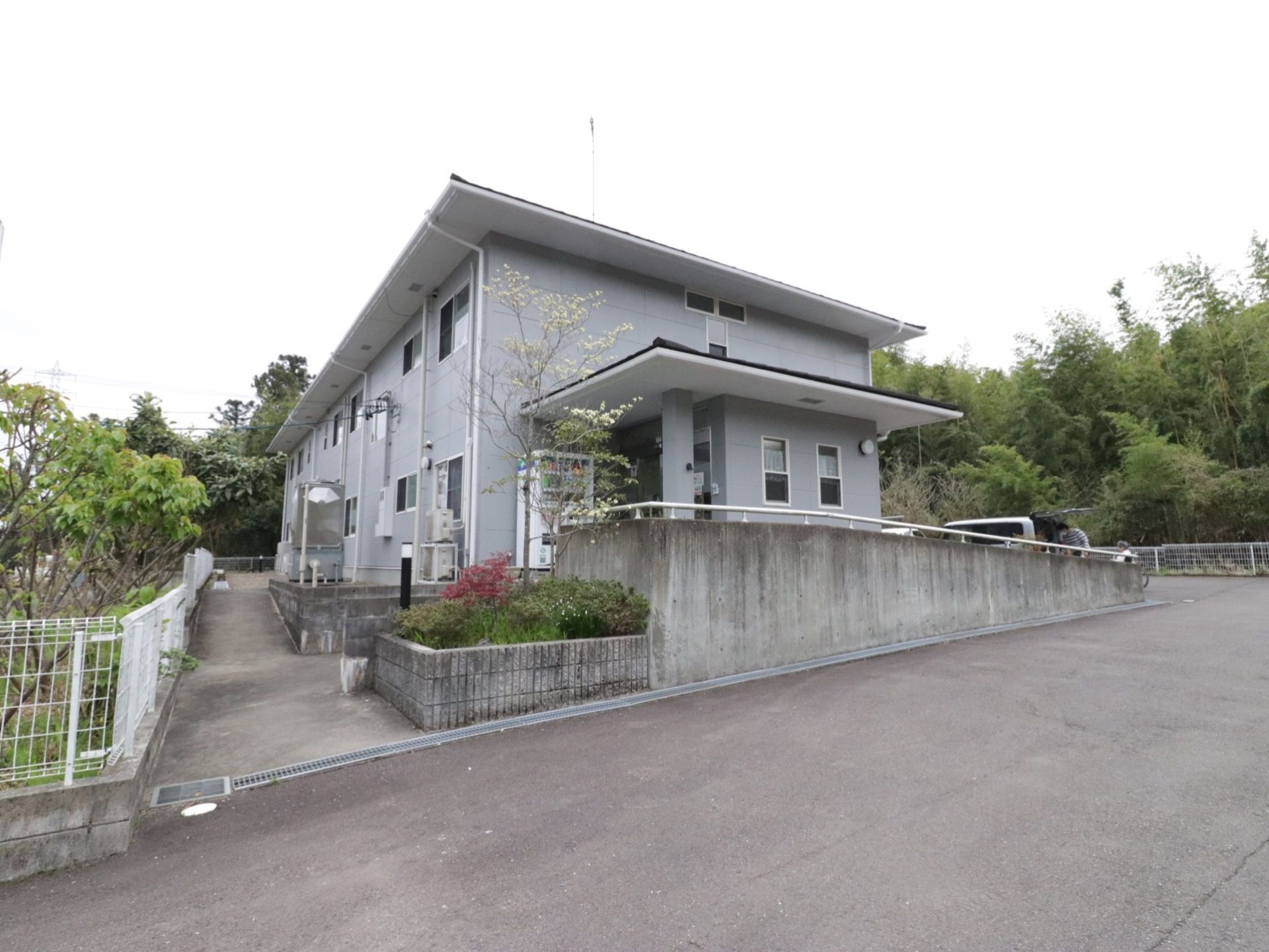 地上から少し坂を上がったところに玄関がある。入口へは階段、またはスロープを使って進む。玄関とスロープの上に屋根がある。