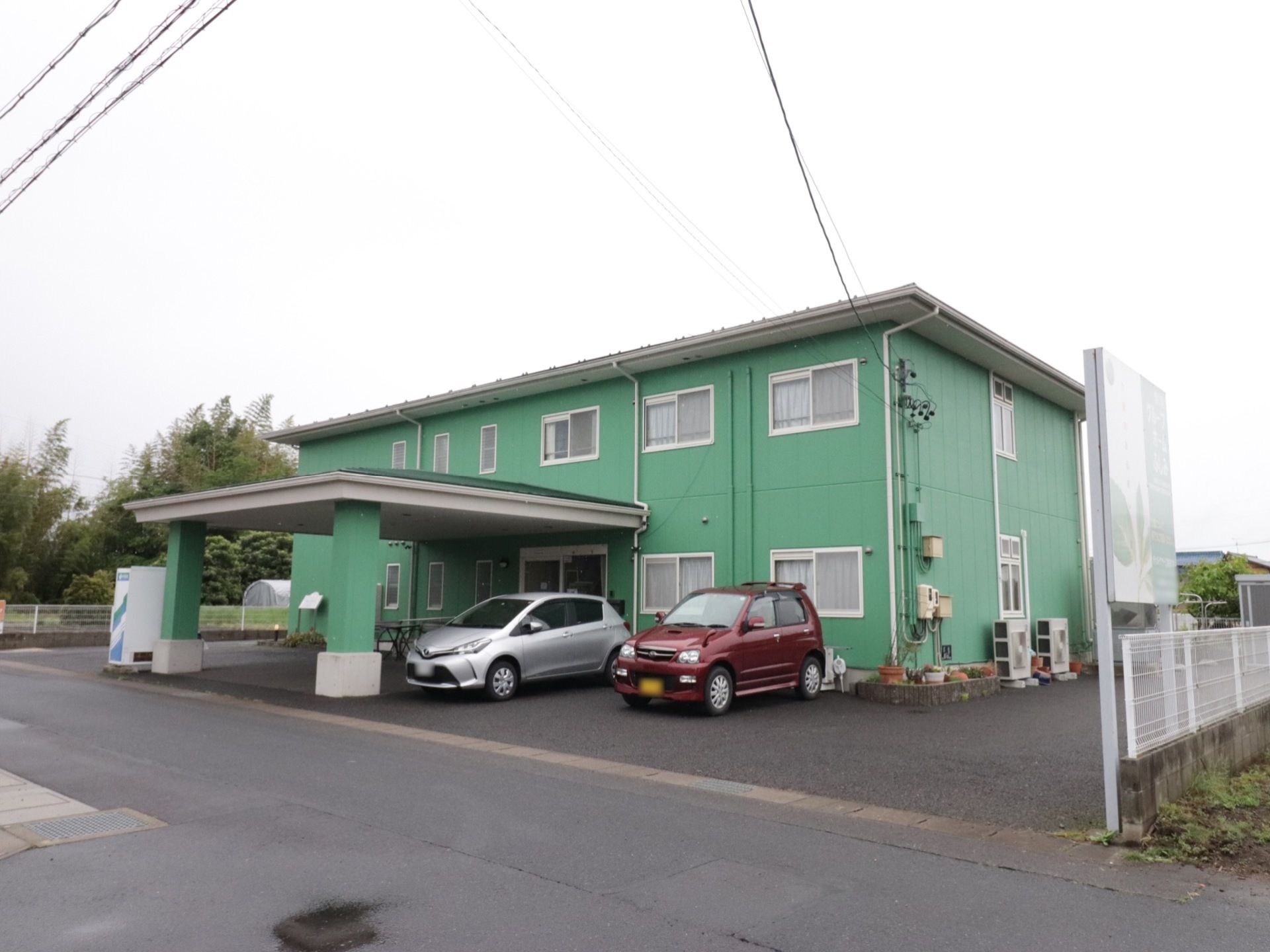 建物は緑色で窓が多くあるのが特徴。入り口には大きな屋根がある。自動車は5～6台停めることができる。自動販売機がある。