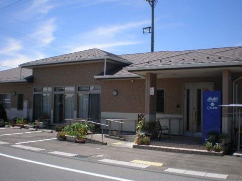 茶色いタイル貼りの外壁に瓦屋根が載っている。玄関前のスロープと階段の周りには花鉢が並んでいる。ひさしの下にはベンチも置いてある。