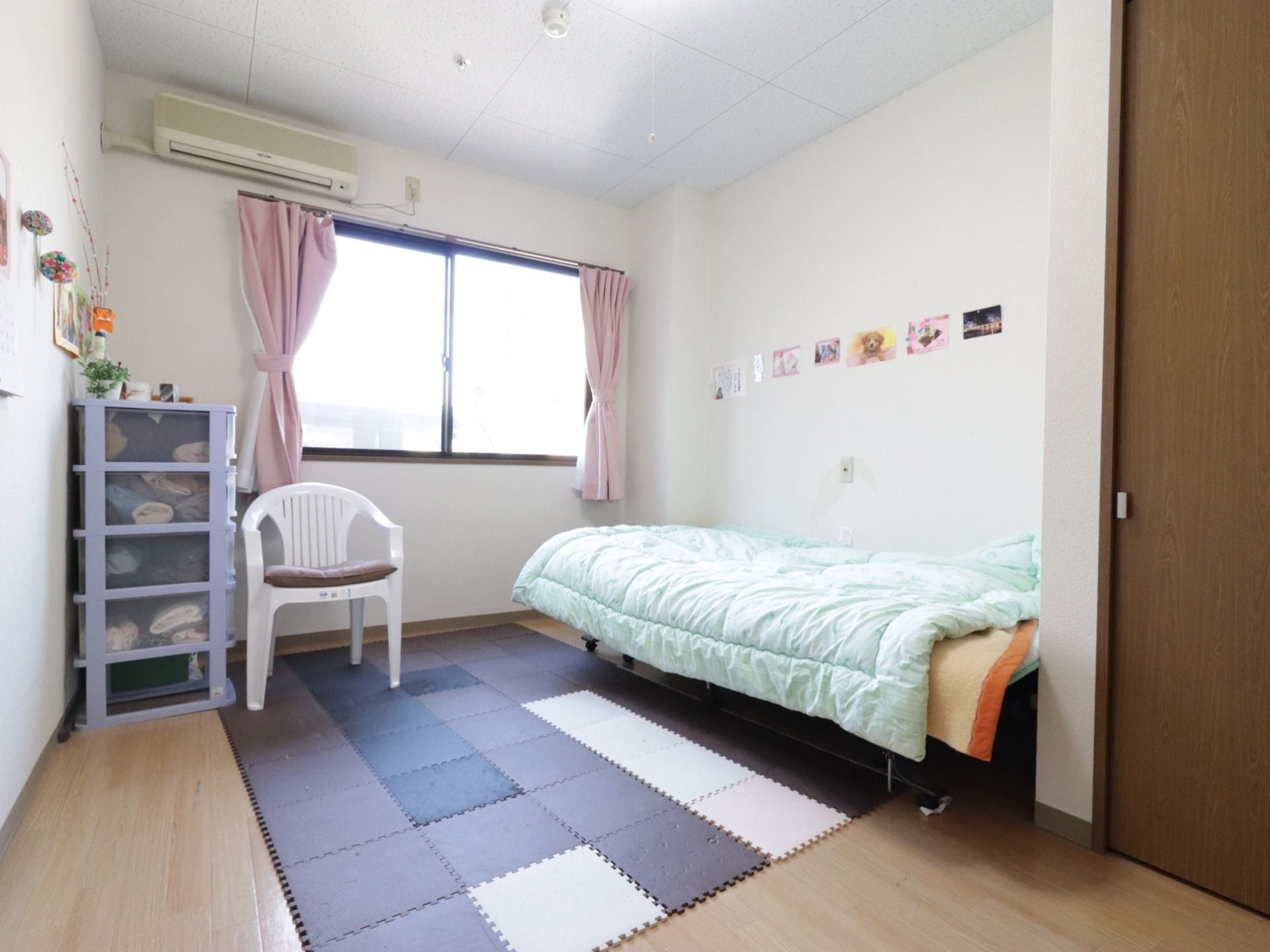 居室には、エアコンやクローゼット、ベッドが備わっている。収納ケースや椅子が置かれている。ジョイントマットが床に敷いてある。