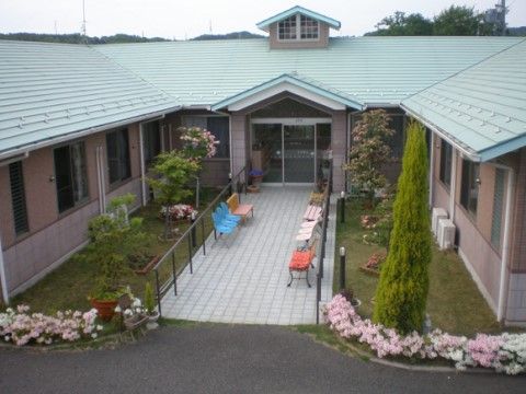 中央に玄関があるコの字型の建物は、玄関前の通路の脇にベンチが並び、建物前の植栽が美しく手入れされている。