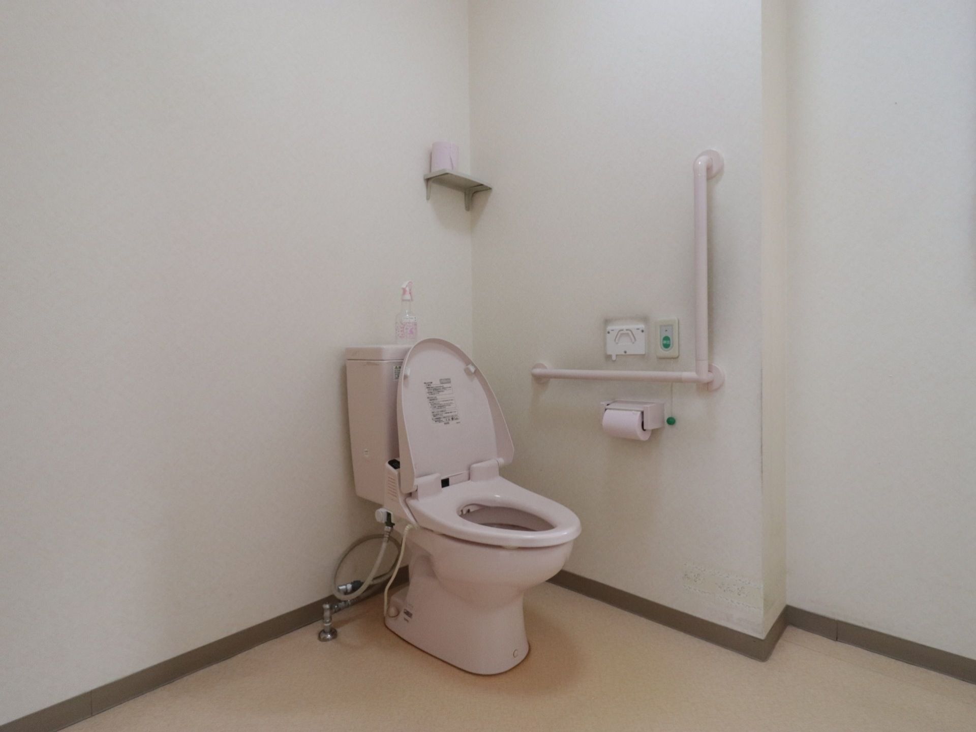 広々としたスペースが確保されたトイレである。L型手すりや呼び出しボタン、備品を置く棚が壁に設置されている。