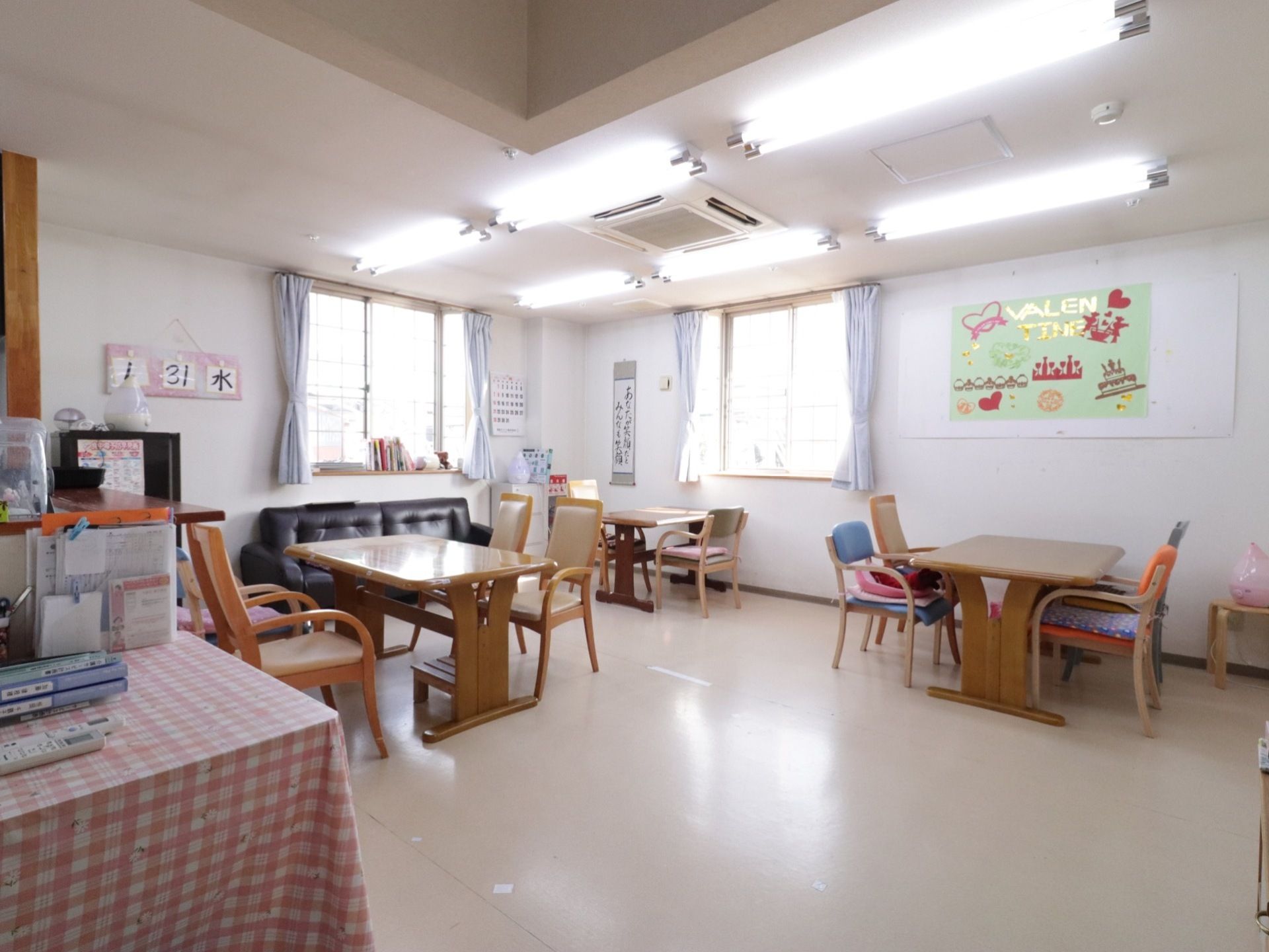 窓から自然光が差し込む明るく広い食堂には、４人掛けのダイニングテーブルやソファが配置されている。加湿器も置かれている。