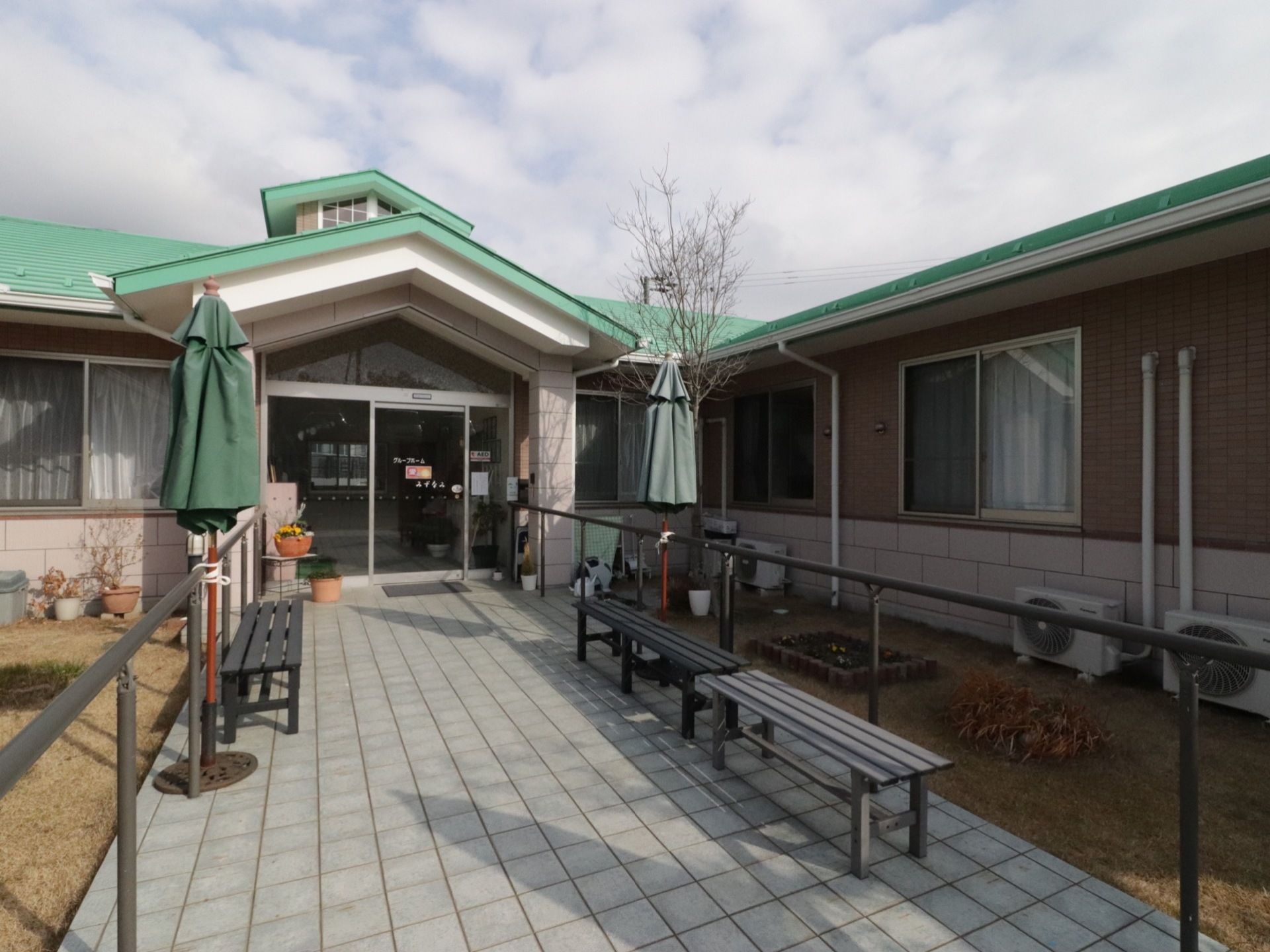 タイル敷きの真っ直ぐなエントランスである。両側には、手すりが取り付けられている。木製ベンチやガーデンパラソルが設置されている。