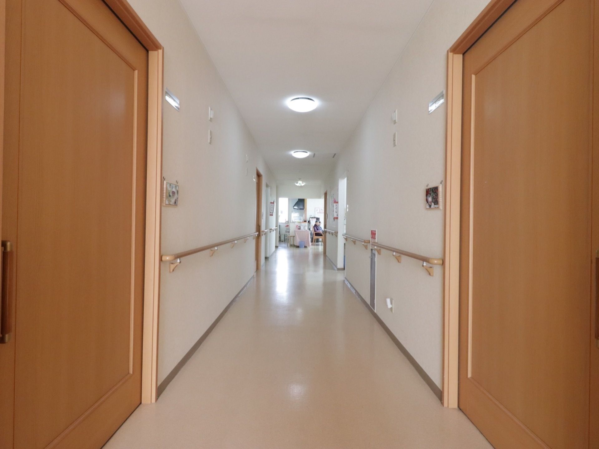 食堂へ続く見通しの良い明るい廊下である。両サイドには、居室の扉が並んでおり、手すりが壁に設置されている。