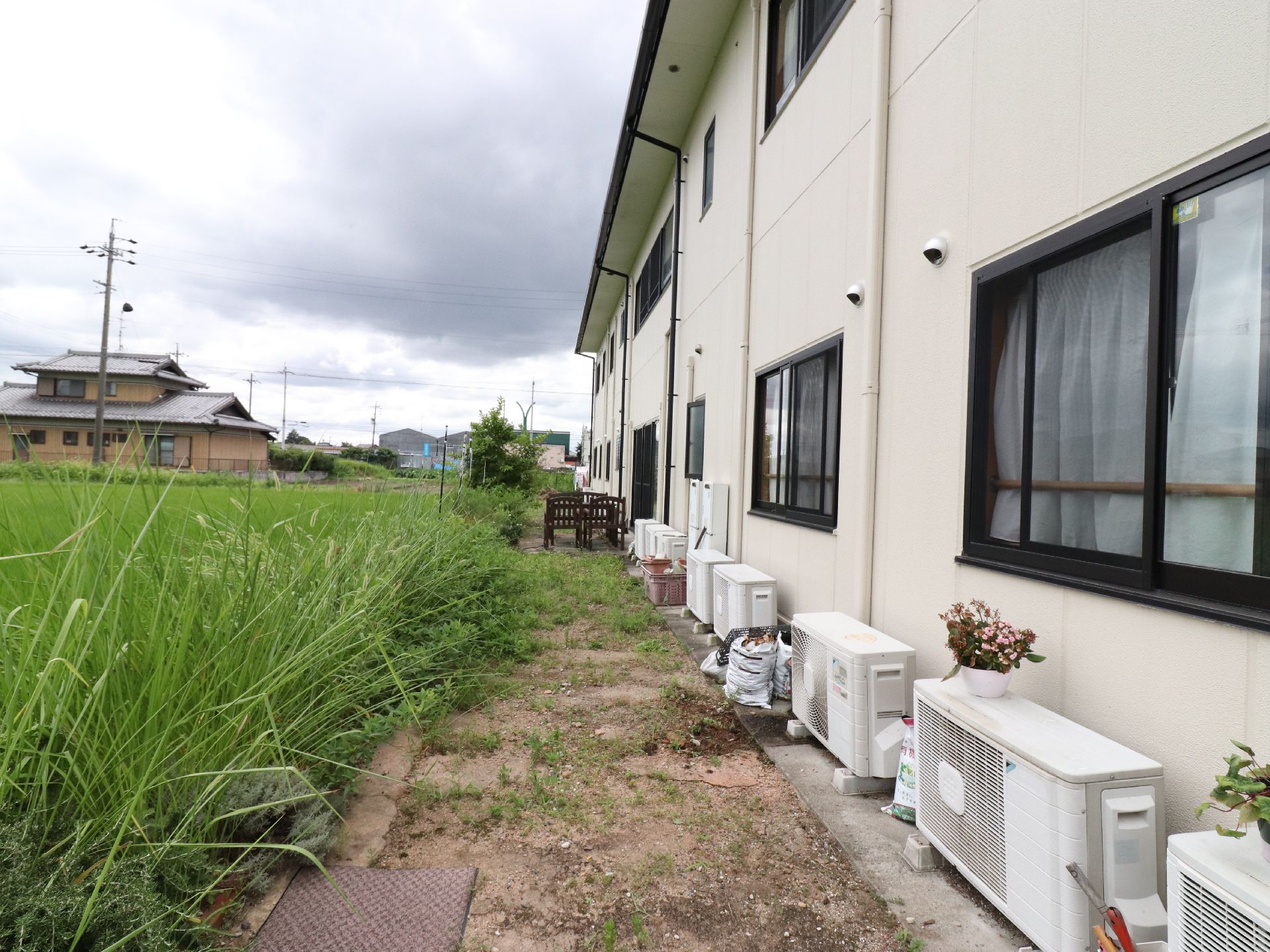 住宅街の中に建っている施設の外観。隣の敷地との間に十分なスペースがあるので安心できる。壁に沿って室外機が置かれている。