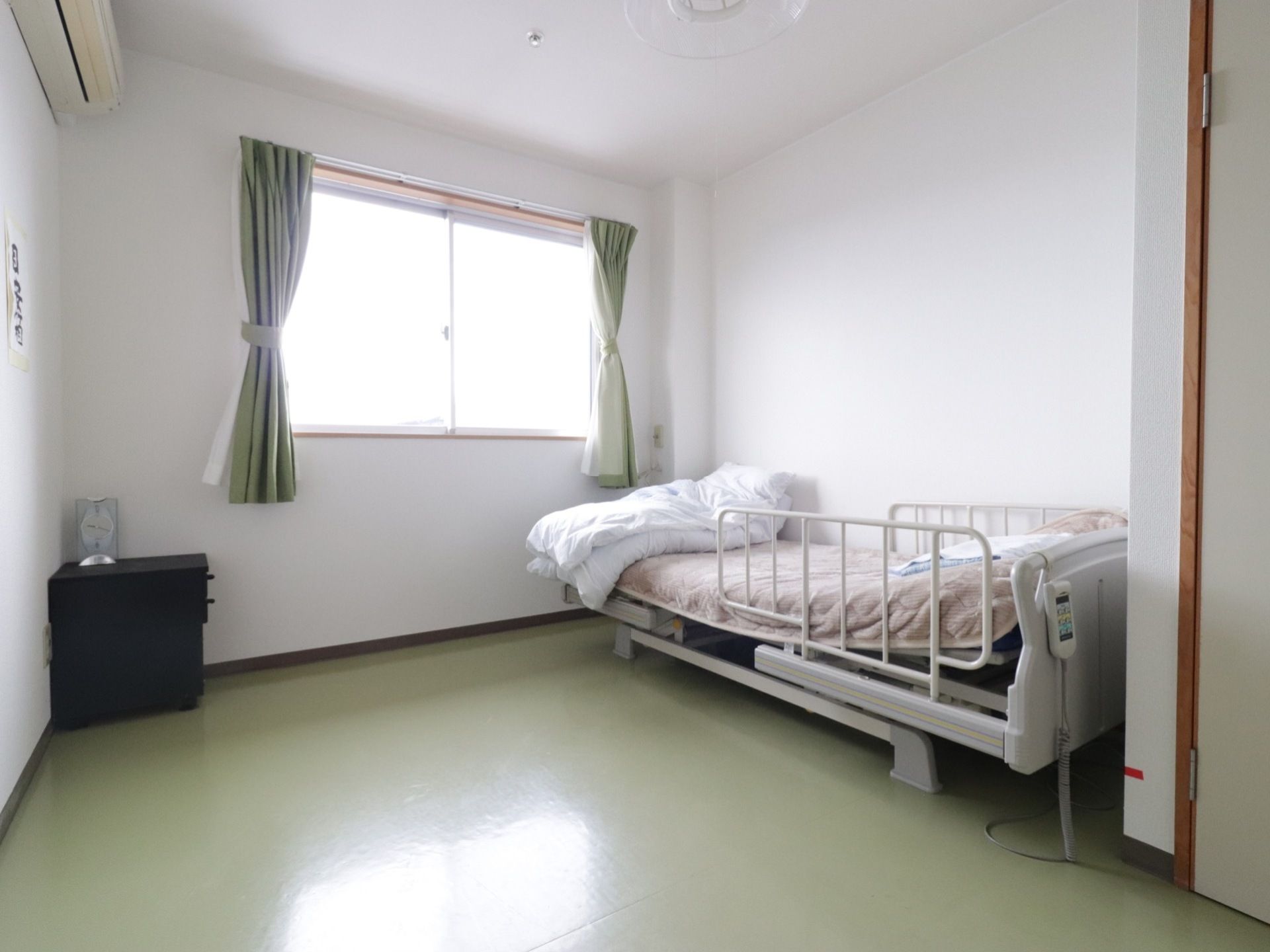 居室には、日差しが差し込む窓が設けられている。介護ベッドやクローゼット、エアコンが完備されている。収納家具が部屋の隅に置かれている。