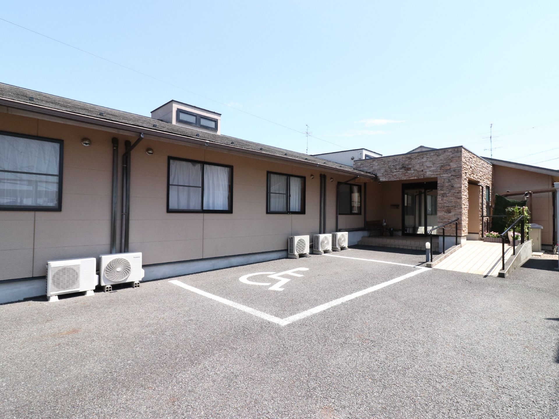 平屋の施設の外観。玄関近くに障害者用駐車場一台分が設けられている。入り口にはスロープと手すりが設置されている。