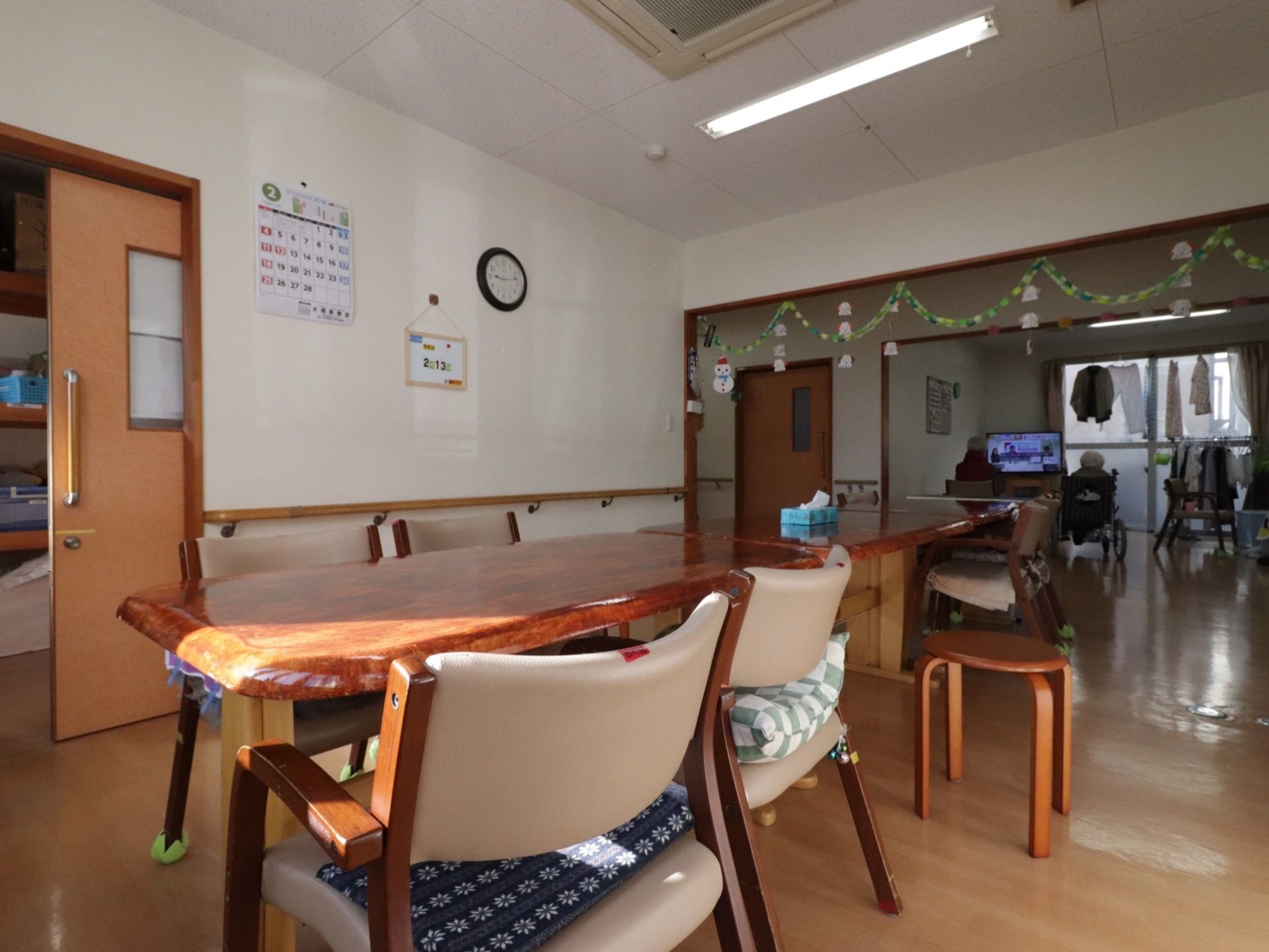 開放的な食堂である。ダイニングテーブルが並べられている。廊下を挟んだ奥のスペースは、リビングになっている。