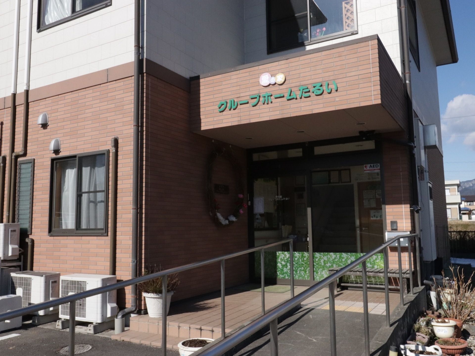 エントランスには、両サイドに手すりを備えたスロープが設けられている。自動ドアの前にベンチが置かれている。