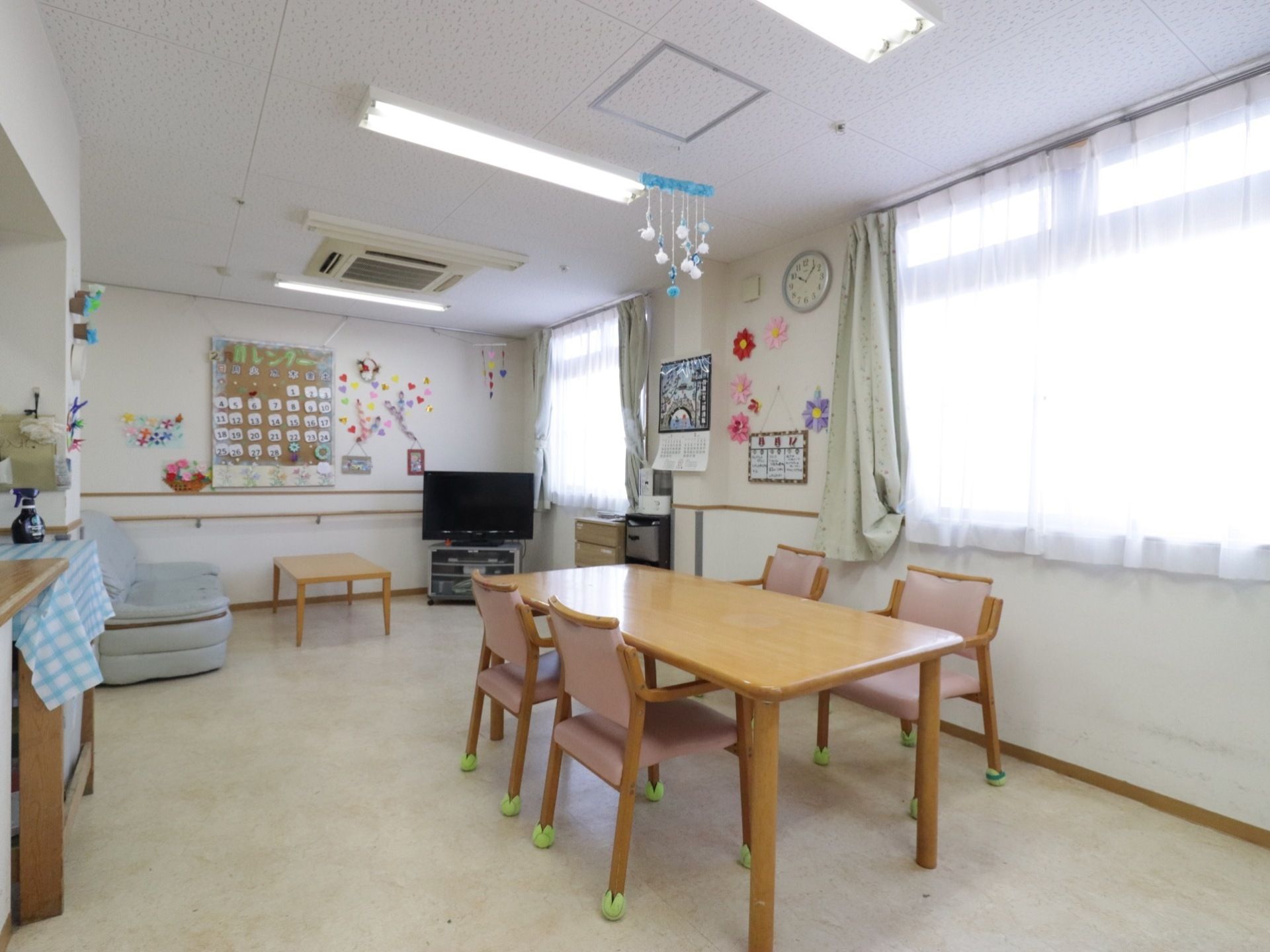 食堂は、明るく広いスペースになっている。４人掛けダイニングテーブルが配置されている。奥の壁際には、大型テレビやソファが置かれている。