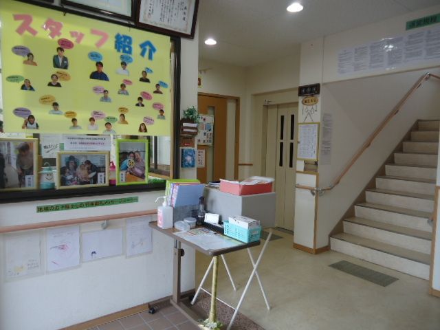 玄関ホールには、階段がある。壁際には、靴箱やベンチが設置されている。マスクや消毒用スプレーが机の上に置かれている。