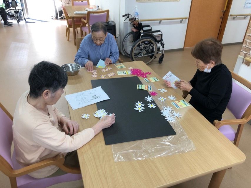 皆様の健康を祈念する千羽鶴も見えるデイルームで、会話している入居者様