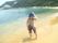 白い砂浜の水際を、帽子を被った女性の入居者様が歩いている。後ろには緑の森と、白い大きな建物が見える。