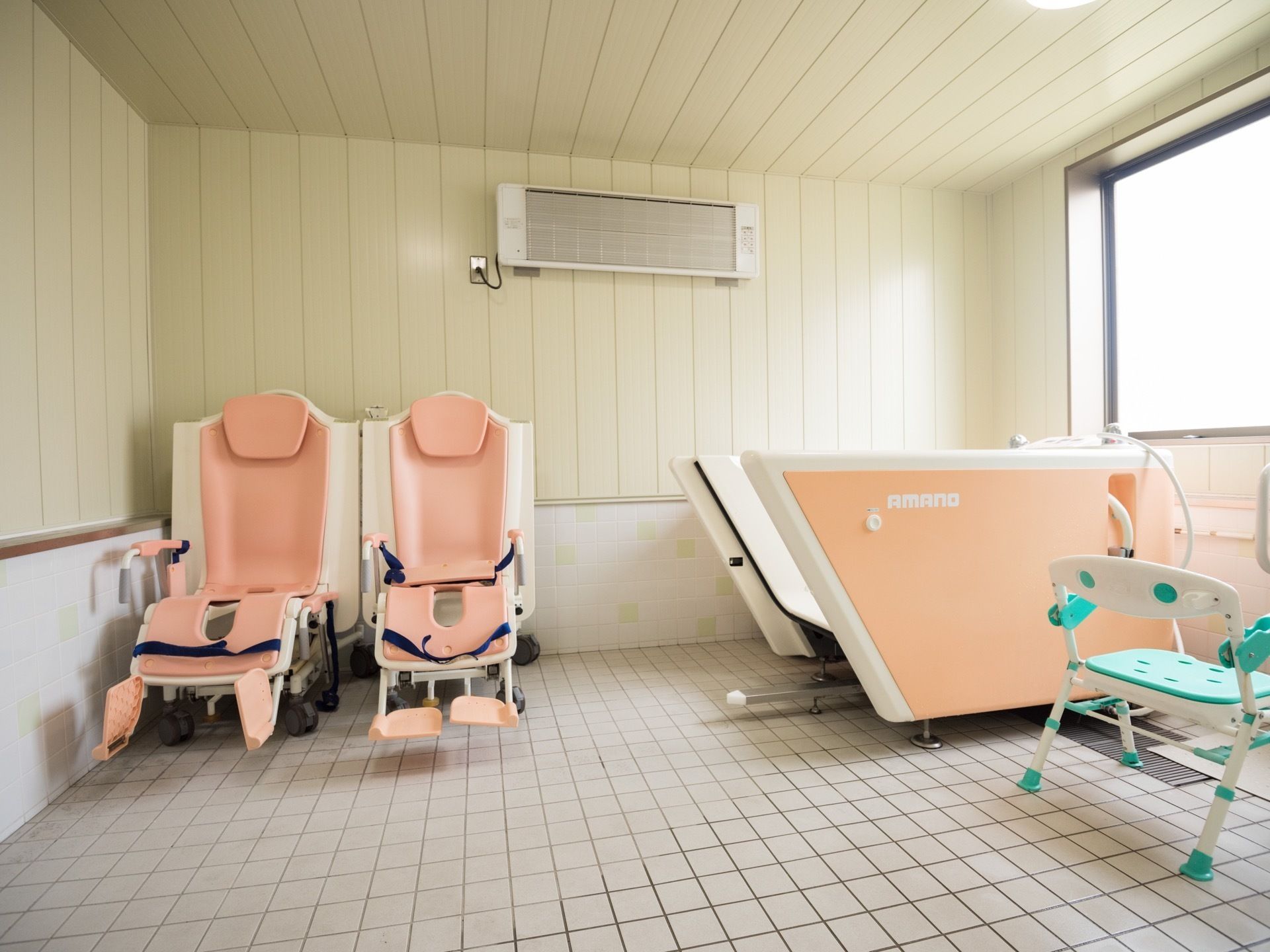 白を基調とした明るい機械浴室で、チェアインタイプの浴槽が設置されている。壁には暖房が取りつけられている。