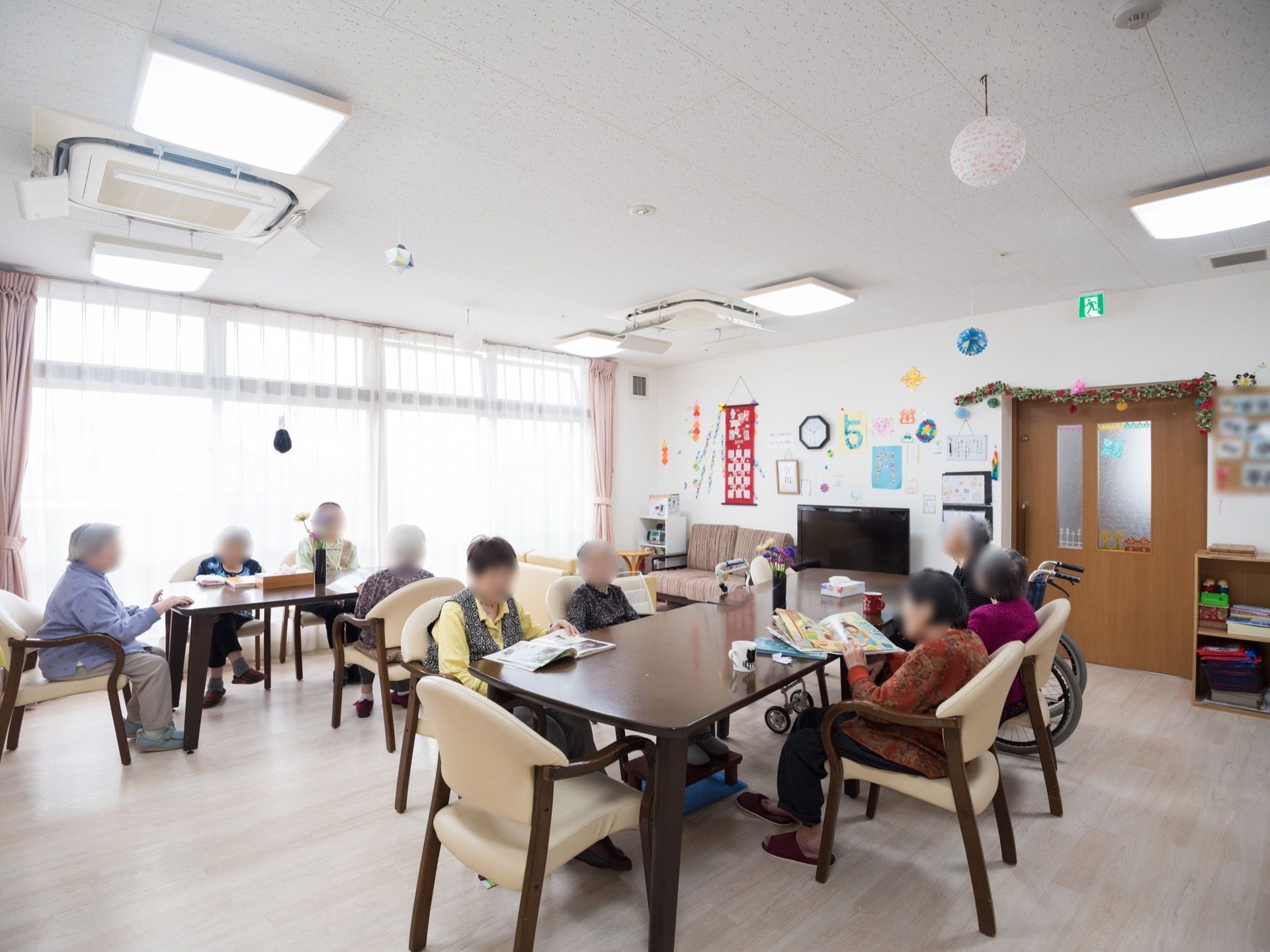入居者様がテレビを観たり、本を読んだりして過ごしている。各ダイニングテーブルの上には花が飾られている。