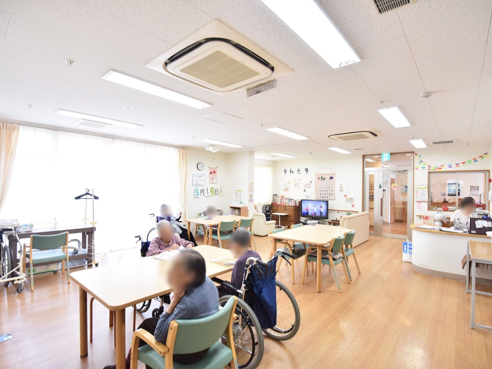 大きな窓があるリビングで、天井に空調設備や蛍光灯が設置されている。窓際にデスクと椅子が１セット置かれている。