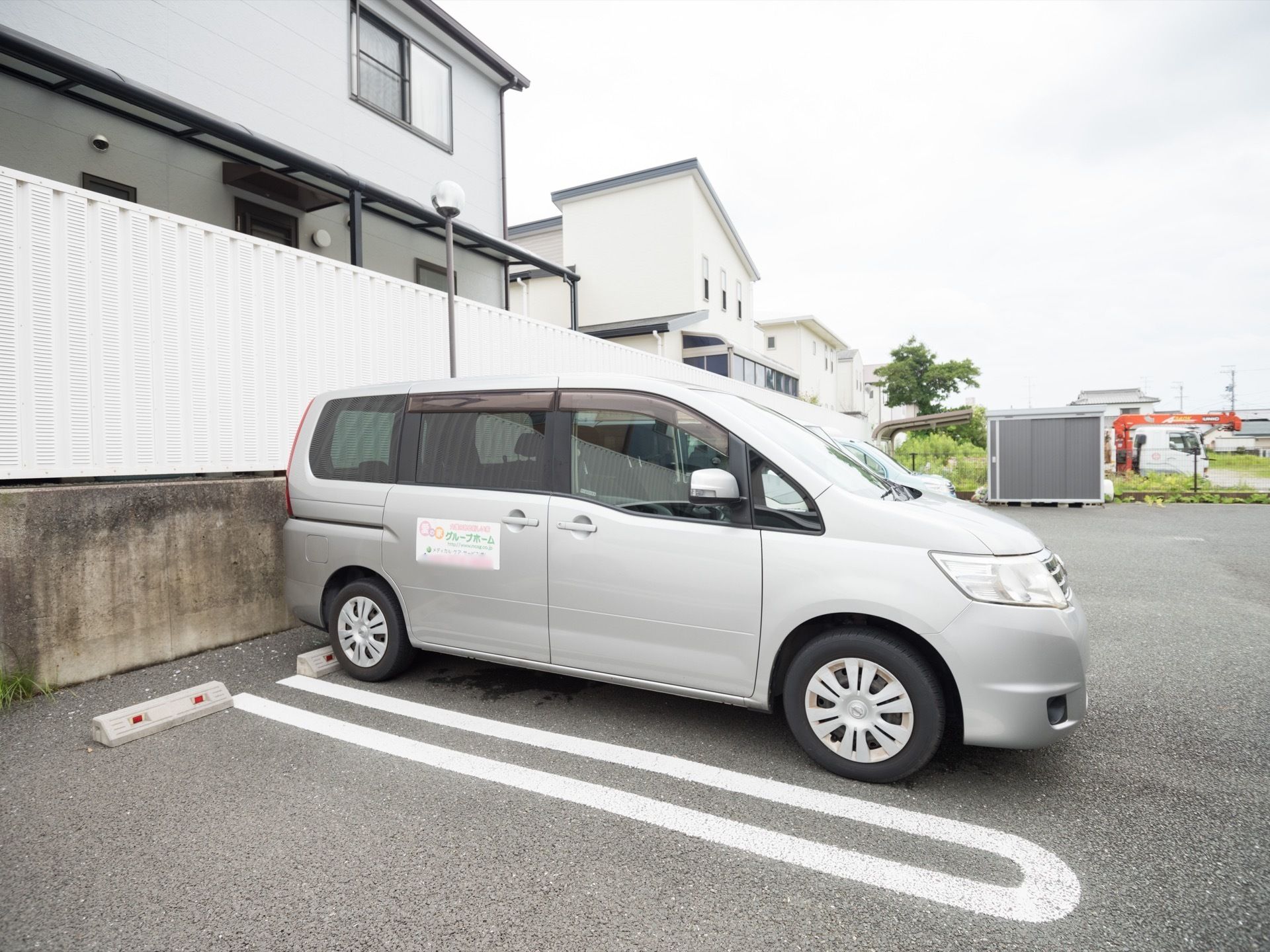 アスファルトに施工された、駐車場がある。白線が引かれている。車止めも備え付けられている。施設専用車がある。