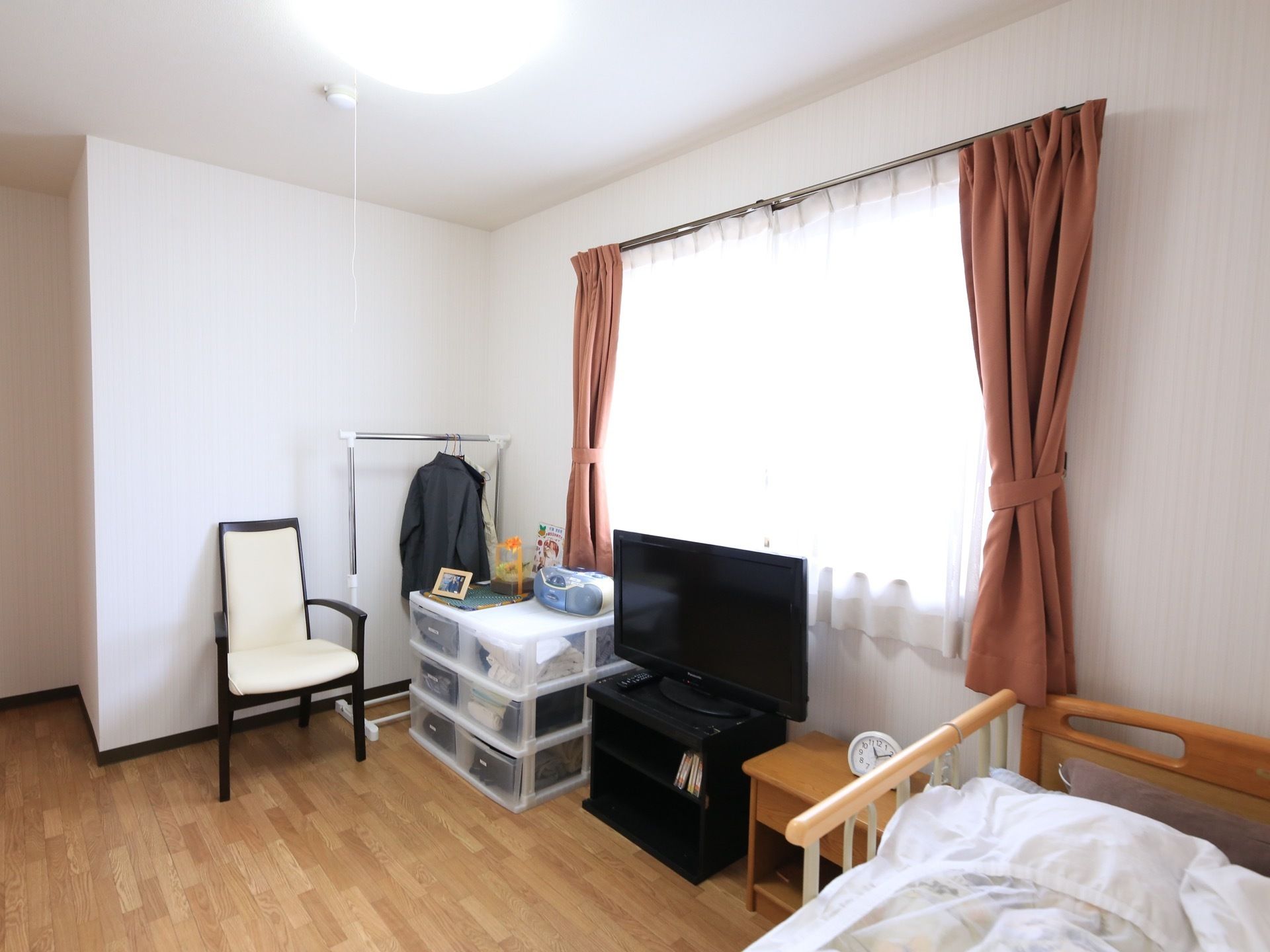 真っ白な壁が清潔感をかもし出している居室である。介護用ベッドや液晶テレビ、椅子、カーテン、LEDライトが完備されている。