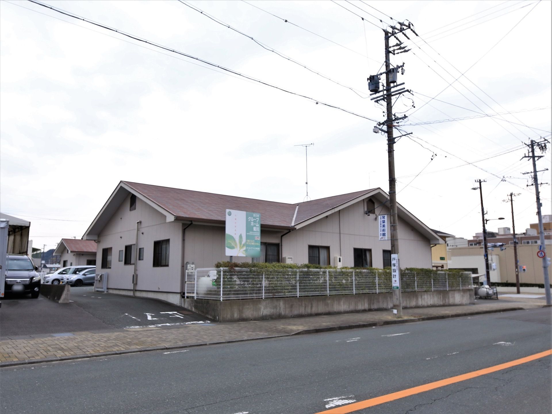 施設の建物の横には道路が通っている。道路から敷地内へは軽い上り坂があり、歩道との境に白い線が引かれている。