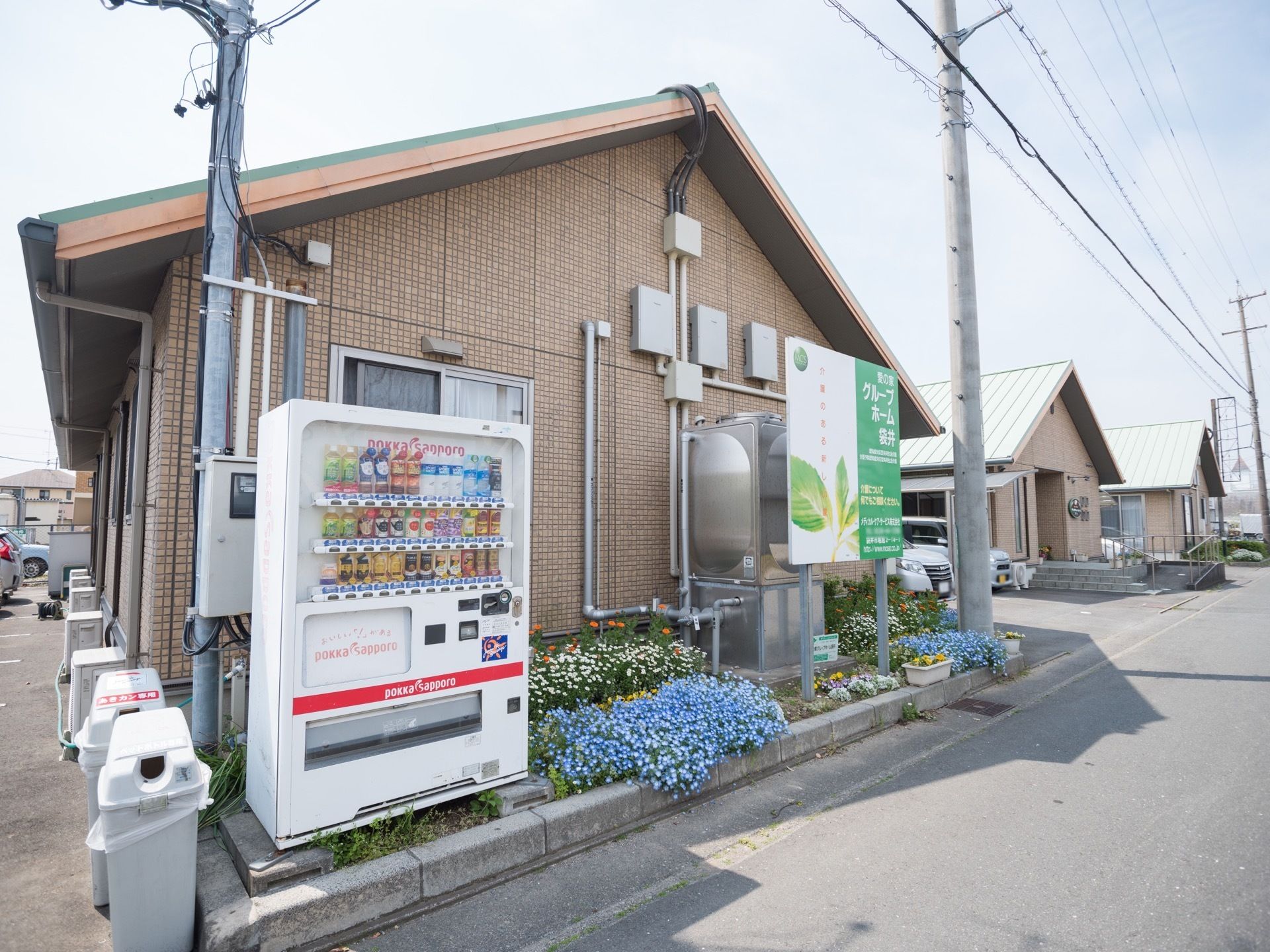 施設は、外壁がブラウンで平屋建ての建物である。周りに花壇があり、きれいな花がたくさん植えられている。