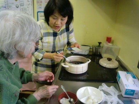 IHコンロの近くでスタッフと一緒に和菓子作りをしている女性入居者様