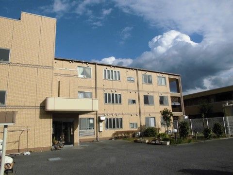 ３階建てのグループホーム。屋根付きの玄関の横には鉢植えが複数置かれており、建物前には中庭が設けられている。