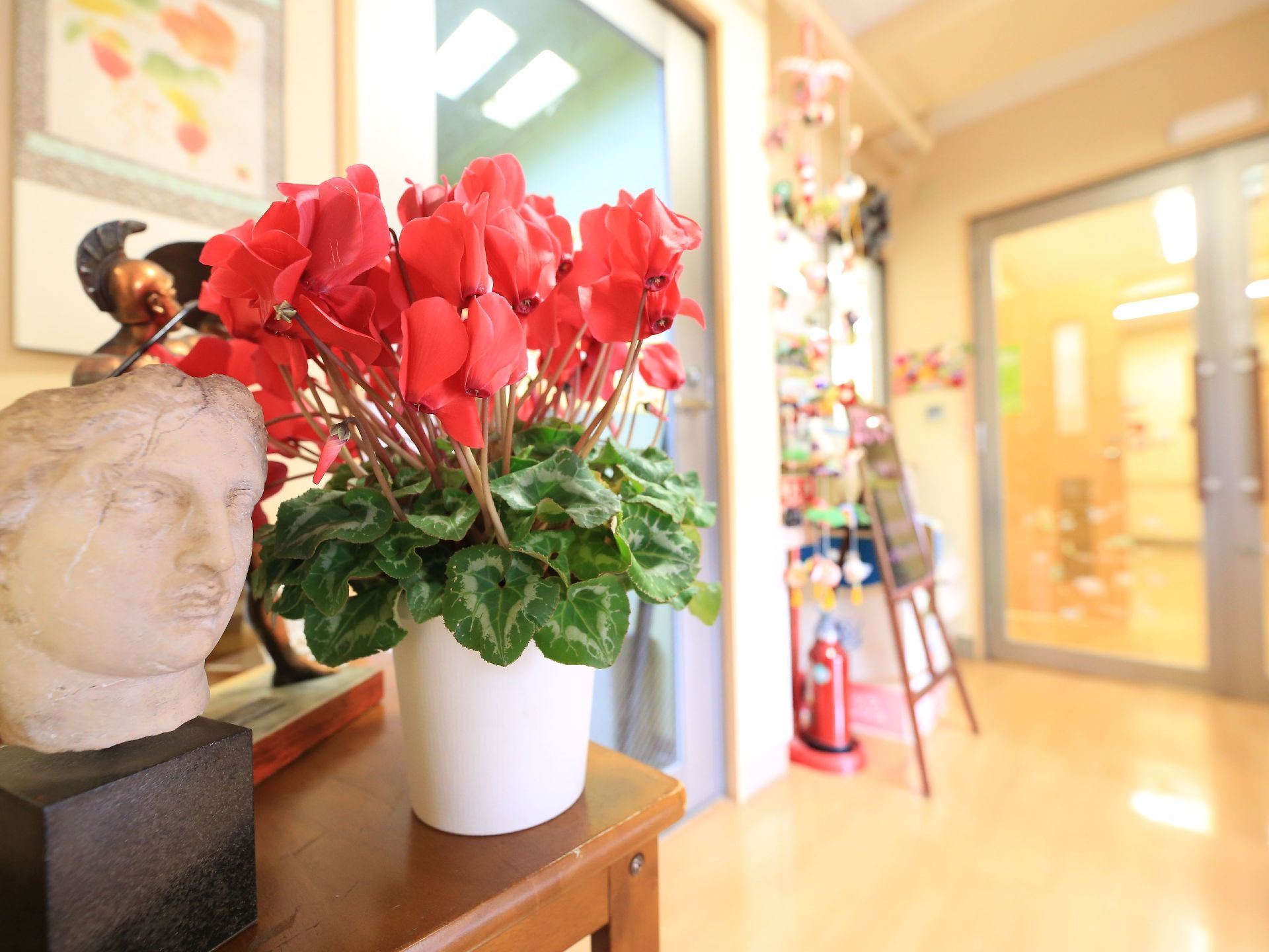 エントランスのテーブルにシクラメンの鉢植えや美術品が置かれている。壁には掛け軸が展示され、華やかな雰囲気である。