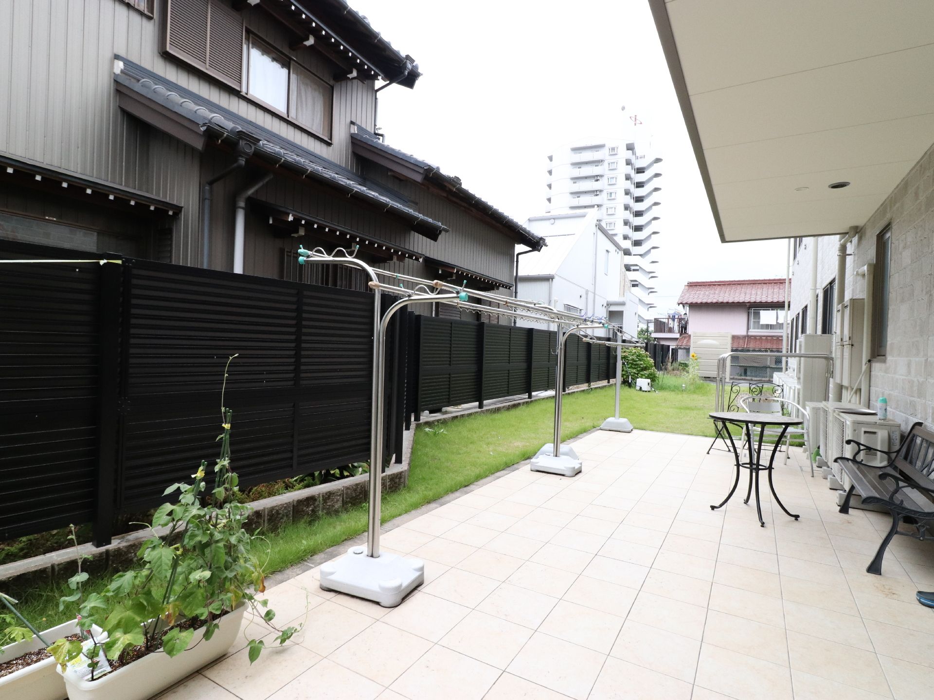 隣の建物に面して設置されたベランダ。洗濯物が干せる設備があり、ベンチも置かれている。プランターが並んでいる。