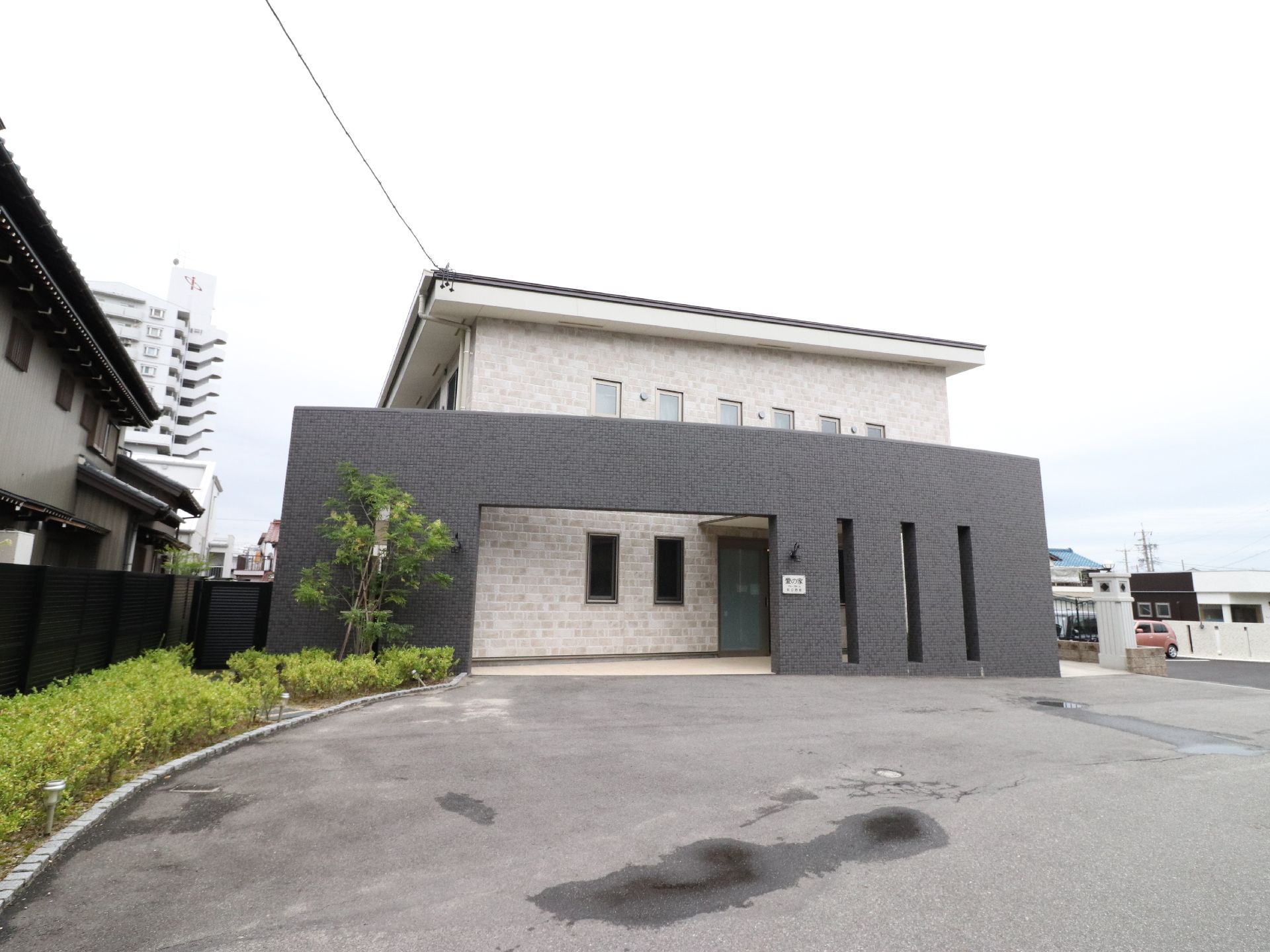 施設の建物を玄関側からとらえたアングル。メインの建造物は薄茶色で、手前には焦げ茶色の外構を建てた構造になっている。