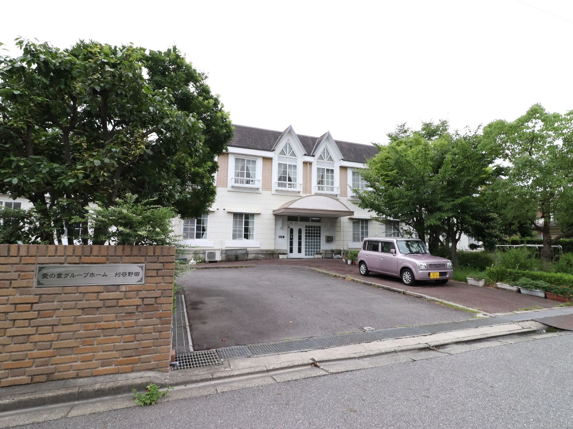 敷地の入り口から臨む施設の全景。立ち木の間に垣間見える三角屋根の洋館は、介護施設とは思えない雰囲気がある。